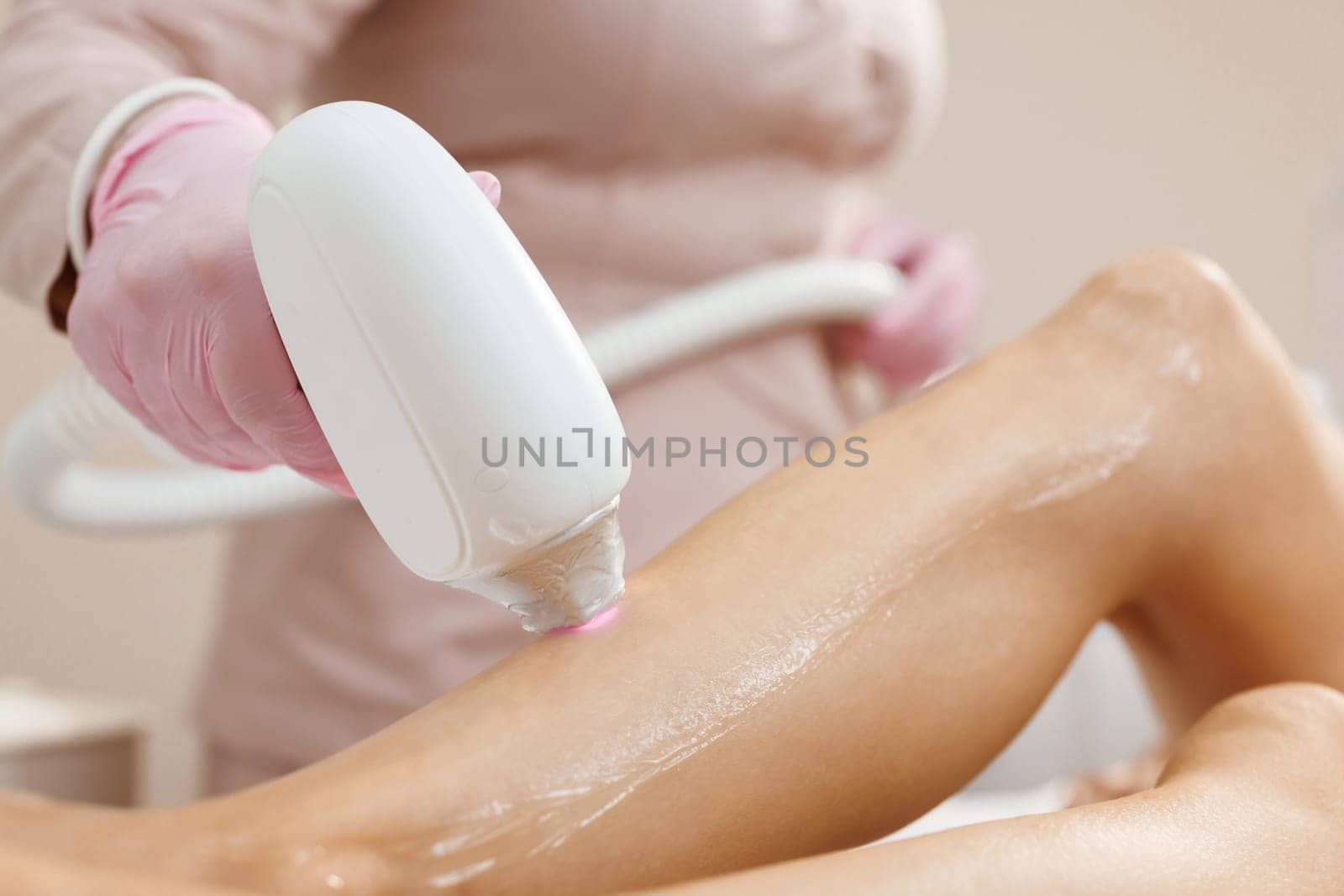 Midsection of female beautician using laser machine on customer's leg at salon. Hair removal on the legs, laser procedure at clinic. Beautician removes hair on beautiful female legs using a laser.