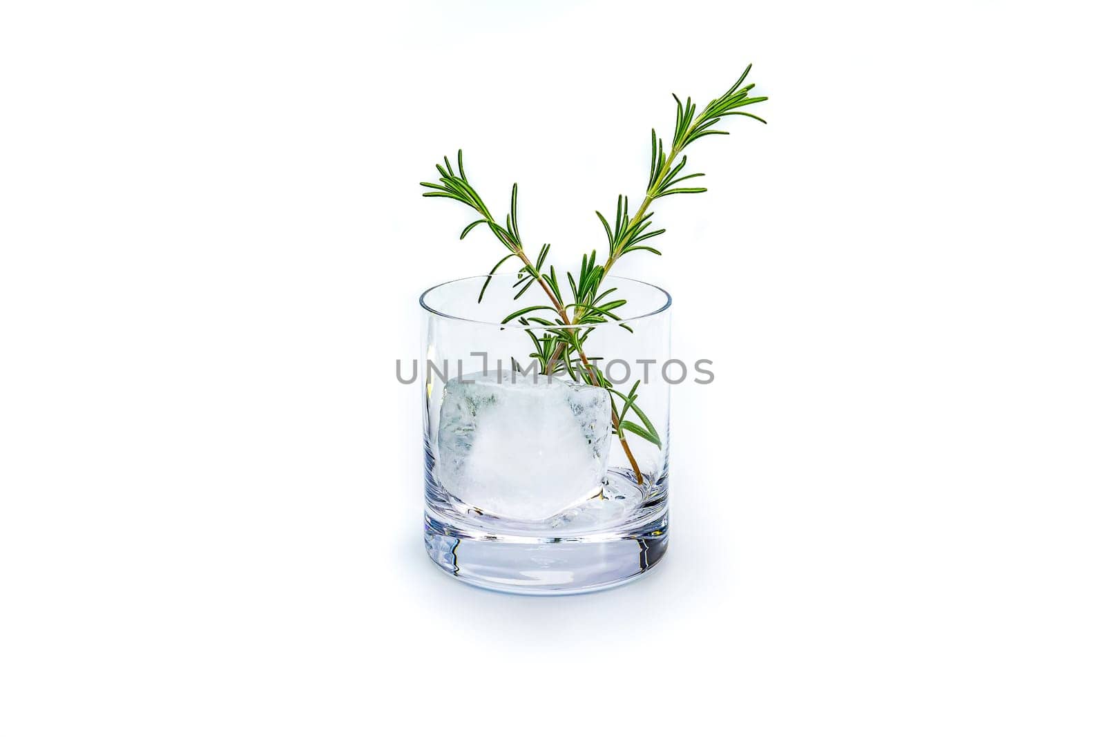 Tumbler glass with a large ice cube and rosemary isolated in the studio