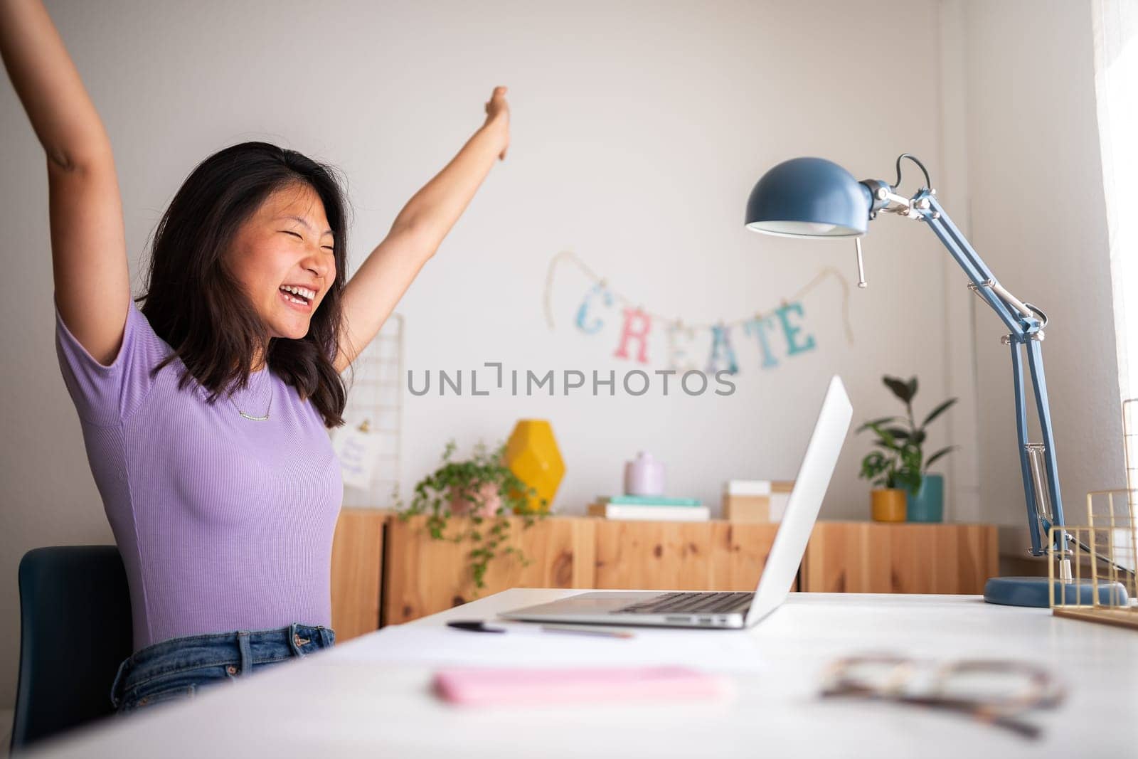 Excited and happy young teen asian female raising arms up celebrating success or achievement at home using laptop. Victory concept.
