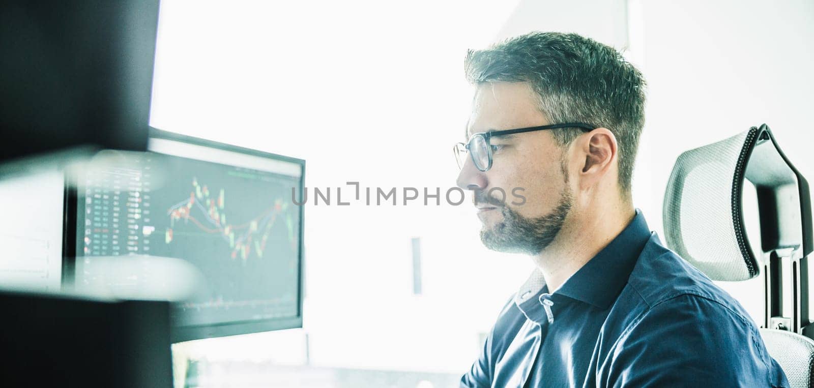 Male stock broker trading online watching charts and data analyses on multiple computer screens.