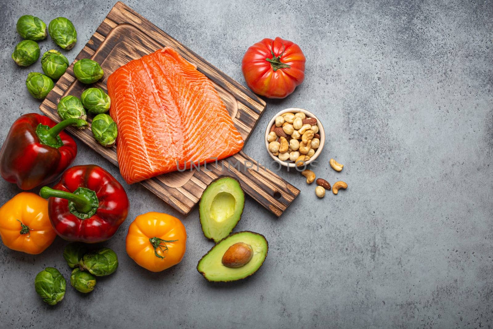 Fresh raw salmon fillet on wooden cutting board, organic bio vegetables and nuts on rustic stone grey background top view. Ingredients full of vitamins for healthy diet and nutrition, space for text