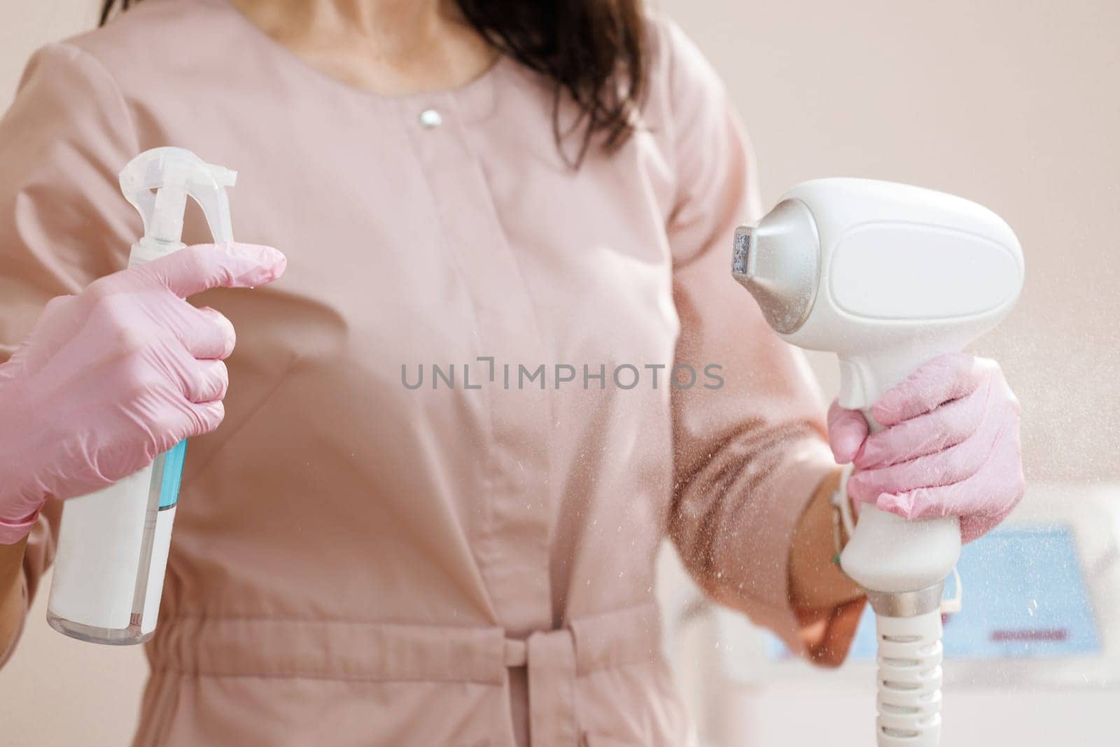 Beautician treats her equipment with an antiseptic. Close up of female beautician in sterile gloves using diode laser hair removal machine. Esthetician preparing equipment for epilation procedure.
