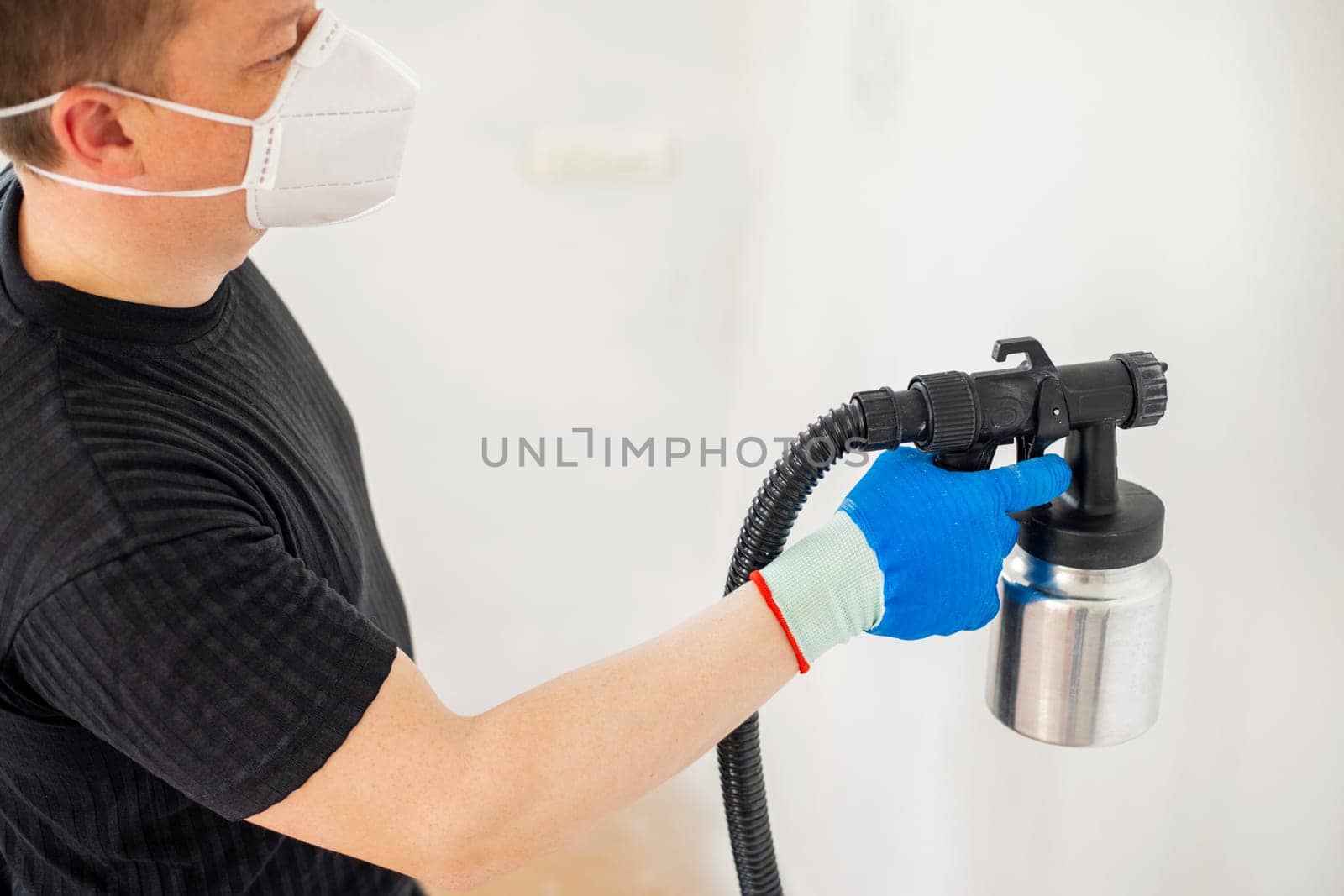 Worker in protective mask painting wall with spray gun. Painting the wall of apartment. Repair concept