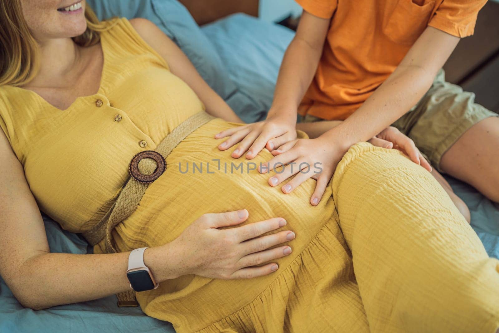 Young pregnant mother hugging her little boy lying in bed at night. Caring and loving parent hugging child.