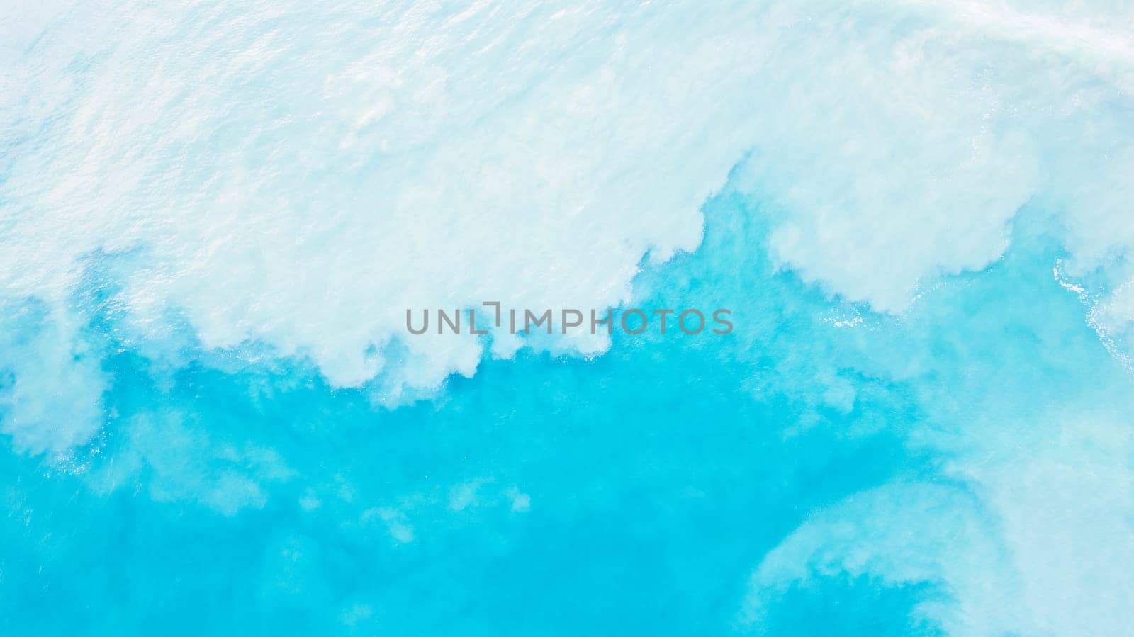 Top view of light blue water with white sand. Waves raise sand and a mix with turquoise water is obtained. Shadows from clouds on a clear ocean. Clear sea. Gradient of blue. The background photo