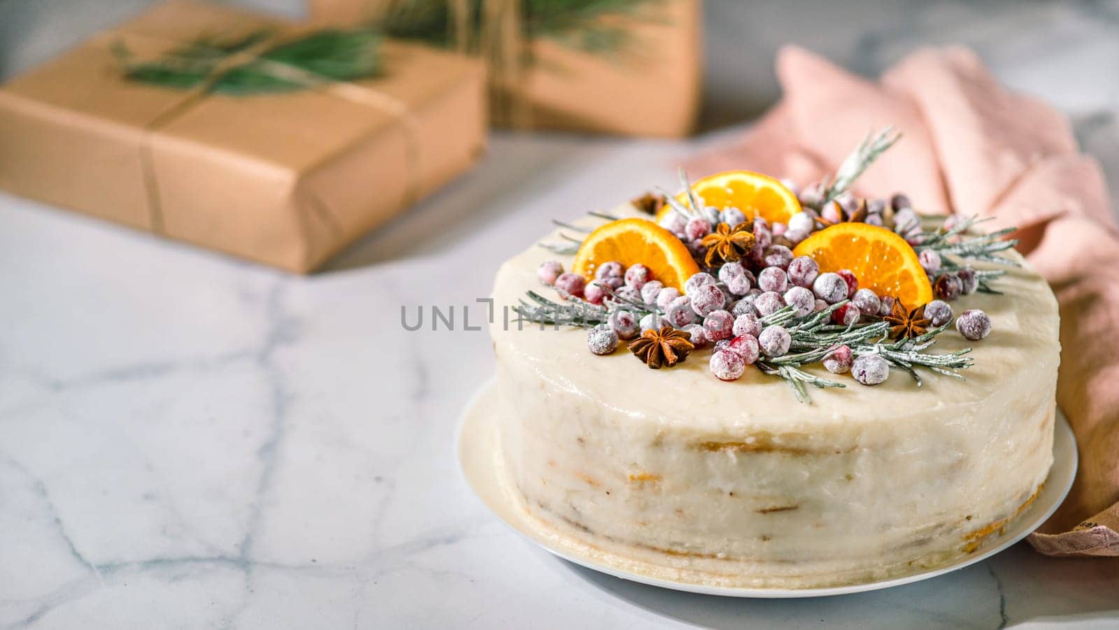 Winter homemade cake on white marble background. White cream christmas cake decored rosemary, cranberries, star anise and oranges slices. Copy space. Vertical