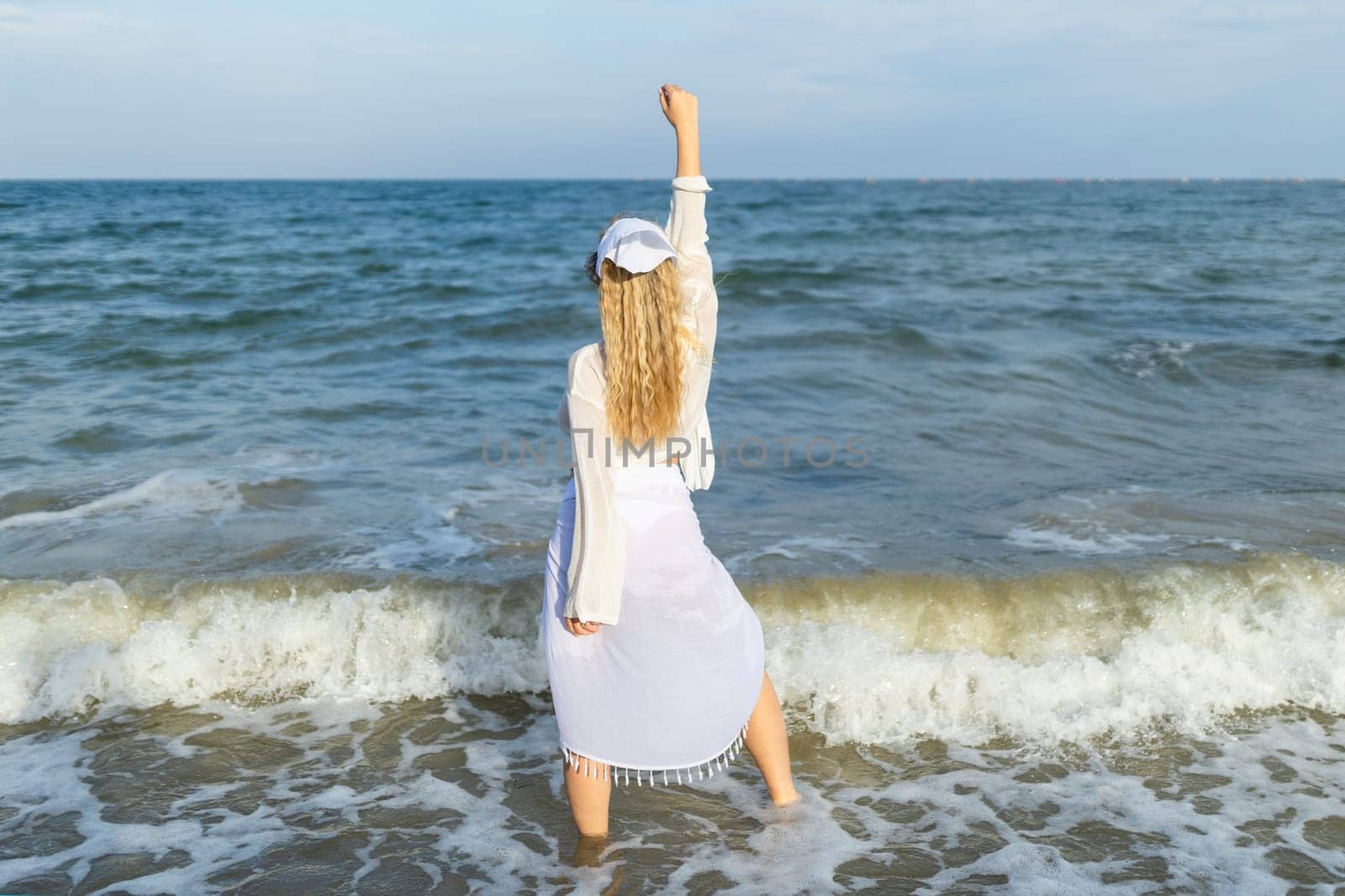 Beautiful girl in the sea. The woman enters the sea. Blue ocean. Girl in a white cape. Beautiful woman on the beach. Summer vacation at sea. The girl loves the sea.