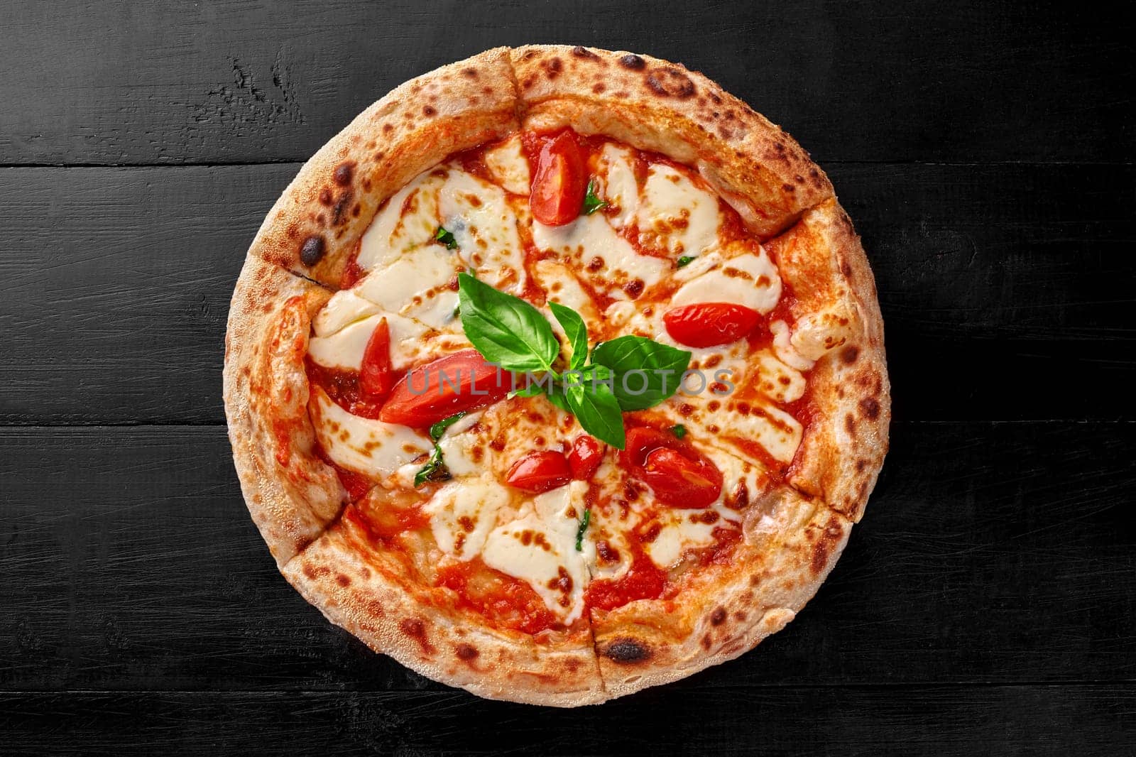 Appetizing traditional Italian pizza Margherita with tomatoes, mozzarella cheese and fresh fragrant green basil on black wooden background, top view. Authentic national cuisine