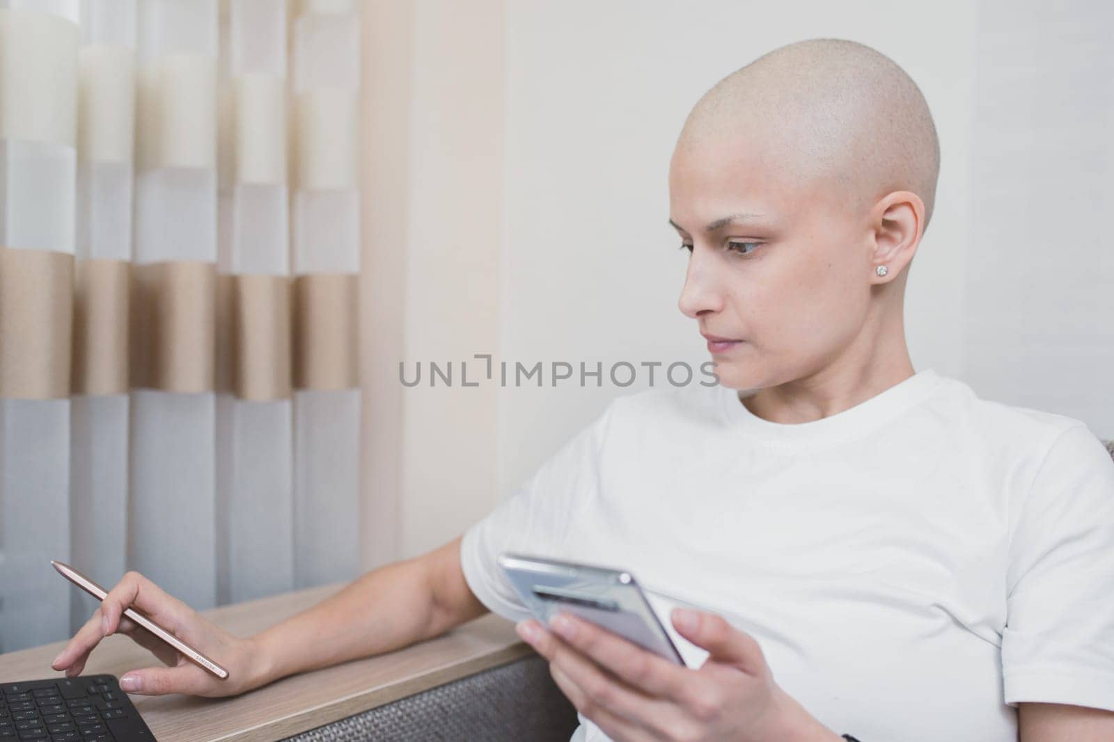 Hairless young woman with oncology, with laptop and smartphone looking for information about the effects of chemotherapy by Rom4ek