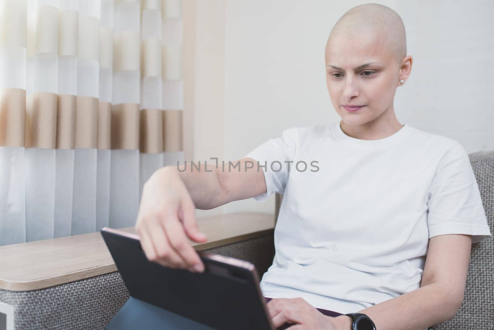 Young bald woman looks at laptop at home, sick leave by Rom4ek