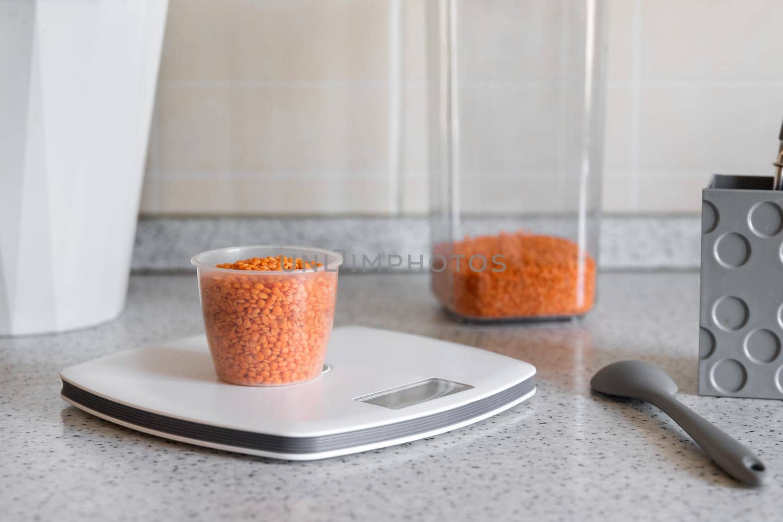 Kitchen scale with measuring cup with red lentils on the kitchen desktop. Concept of a healthy diet or diet for weight loss by Rom4ek