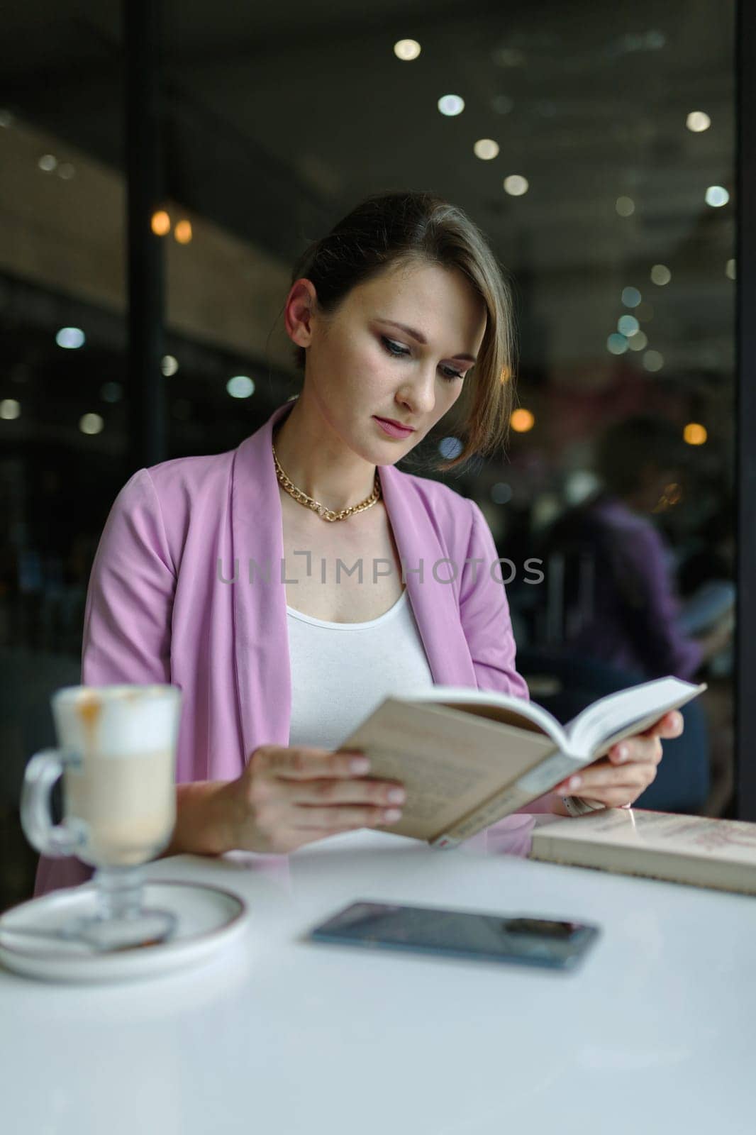 Young cute caucasian woman reading a book in a cafe, copy space, vertical.