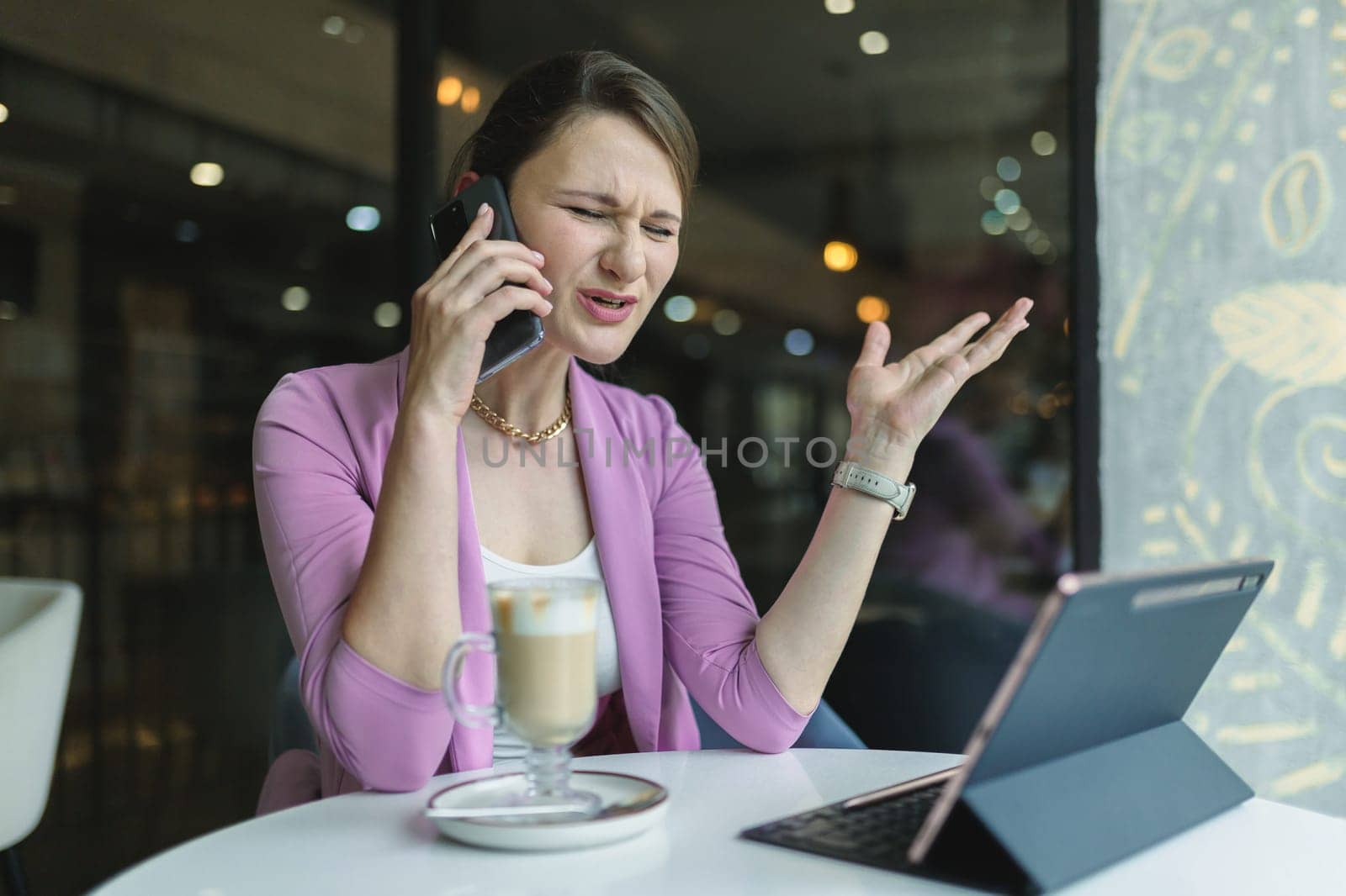 Upset young business woman emotionally talking on the phone in a cafe by Rom4ek
