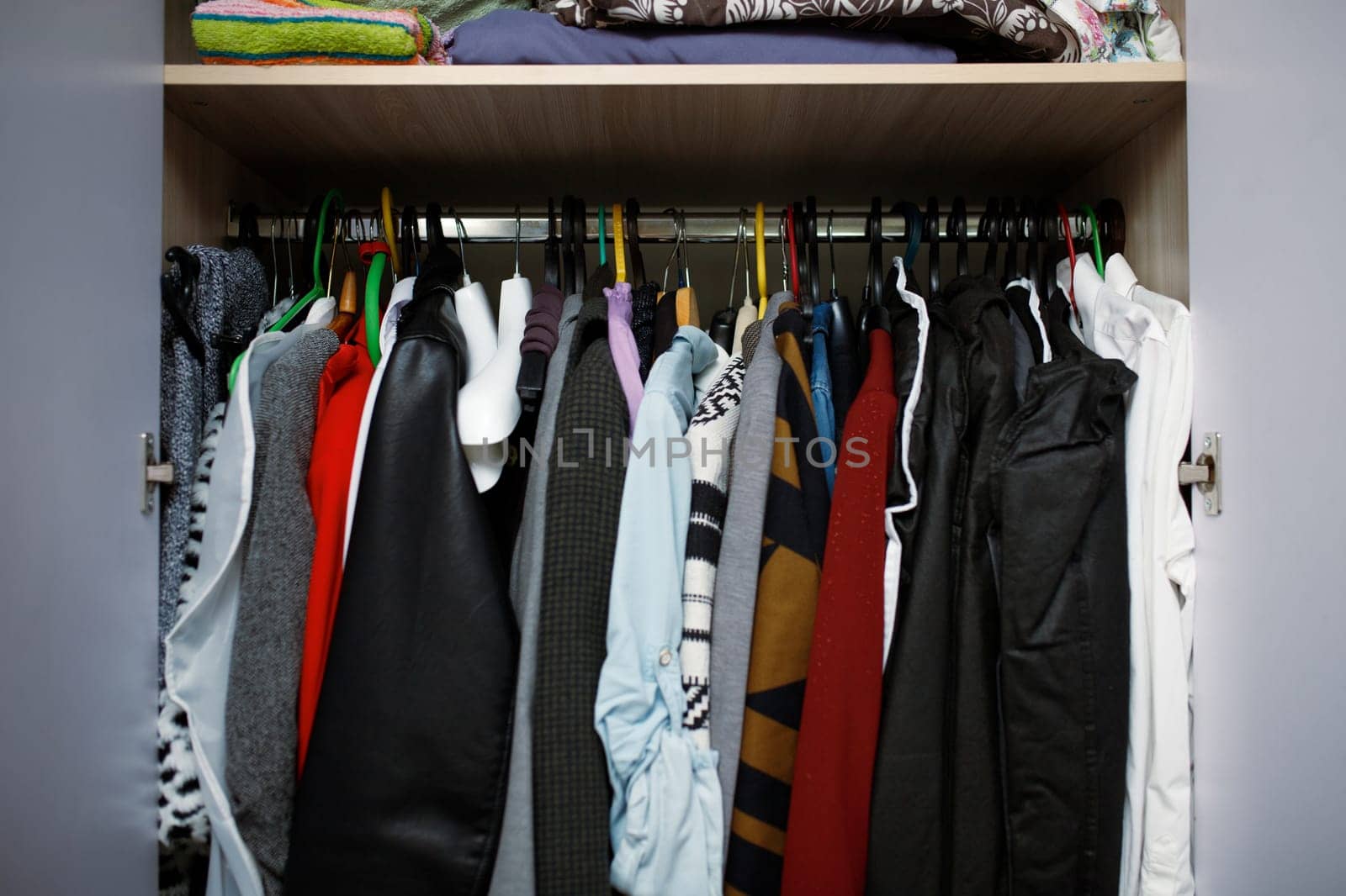 Open closet with a variety of clothes hanging randomly on hangers.