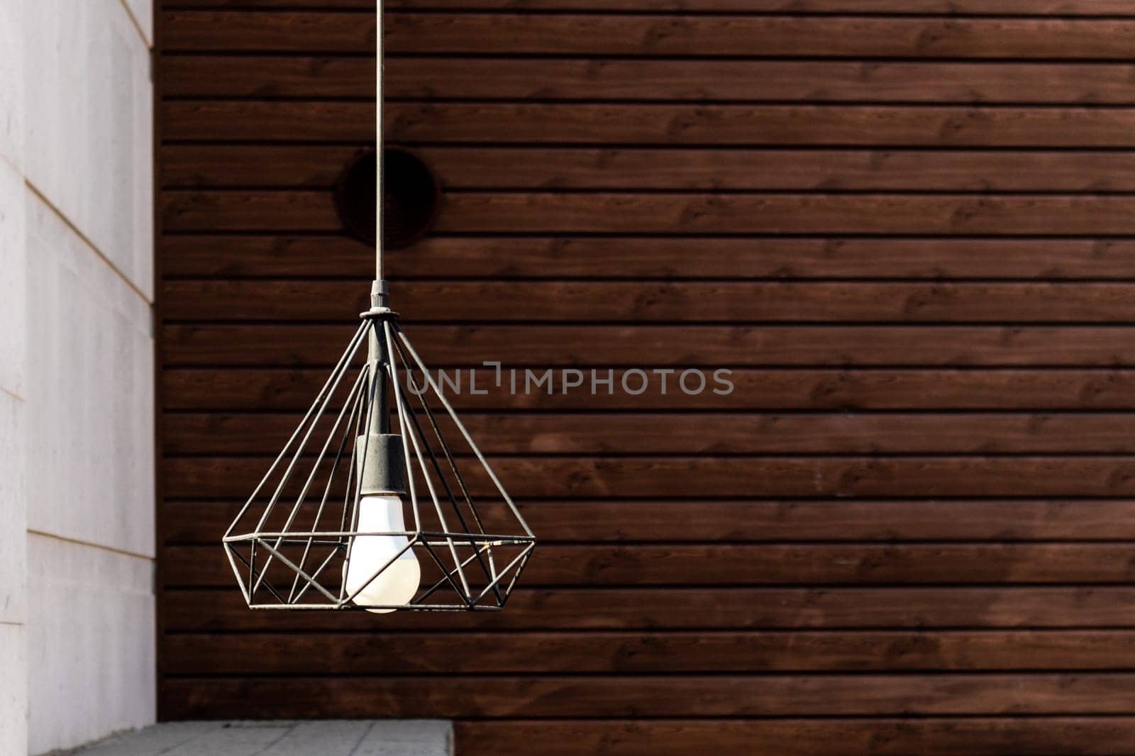 Modern garden pendant lamp hanging on the outdoor terrace during on wooden wall background.