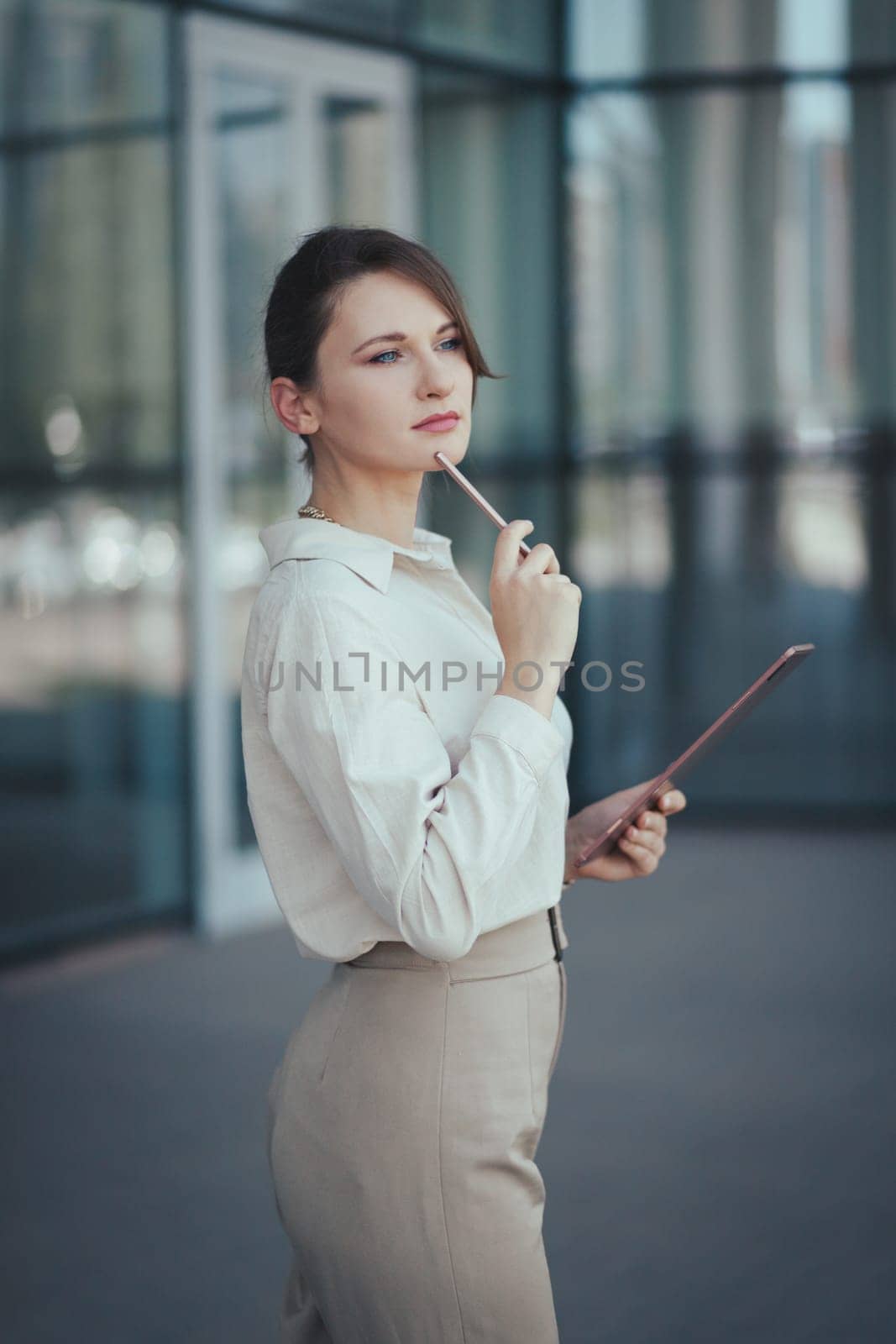 Business portrait of a young caucasian woman with a tablet in her hands against the backdrop of a business center, vertical.