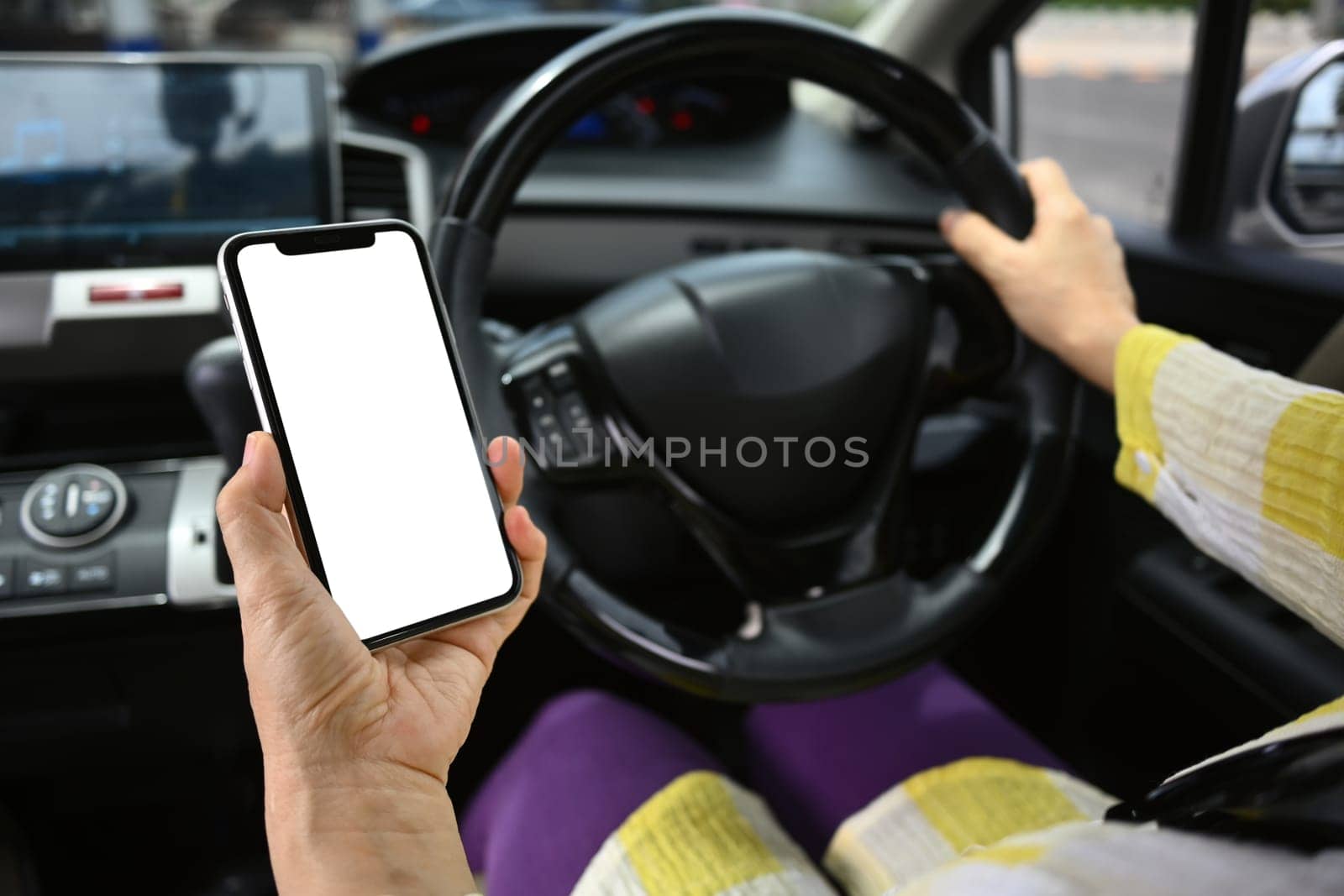 Closeup shot of senior woman hand using mobile phone while driving a car. Unsafe driving and gadgets concept.