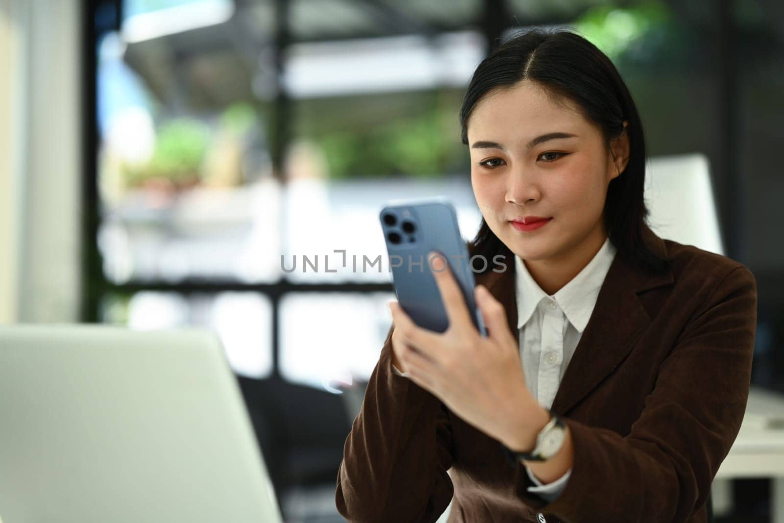 Attractive businesswoman checking social media on smartphone at office desk. People, technology and lifestyle.