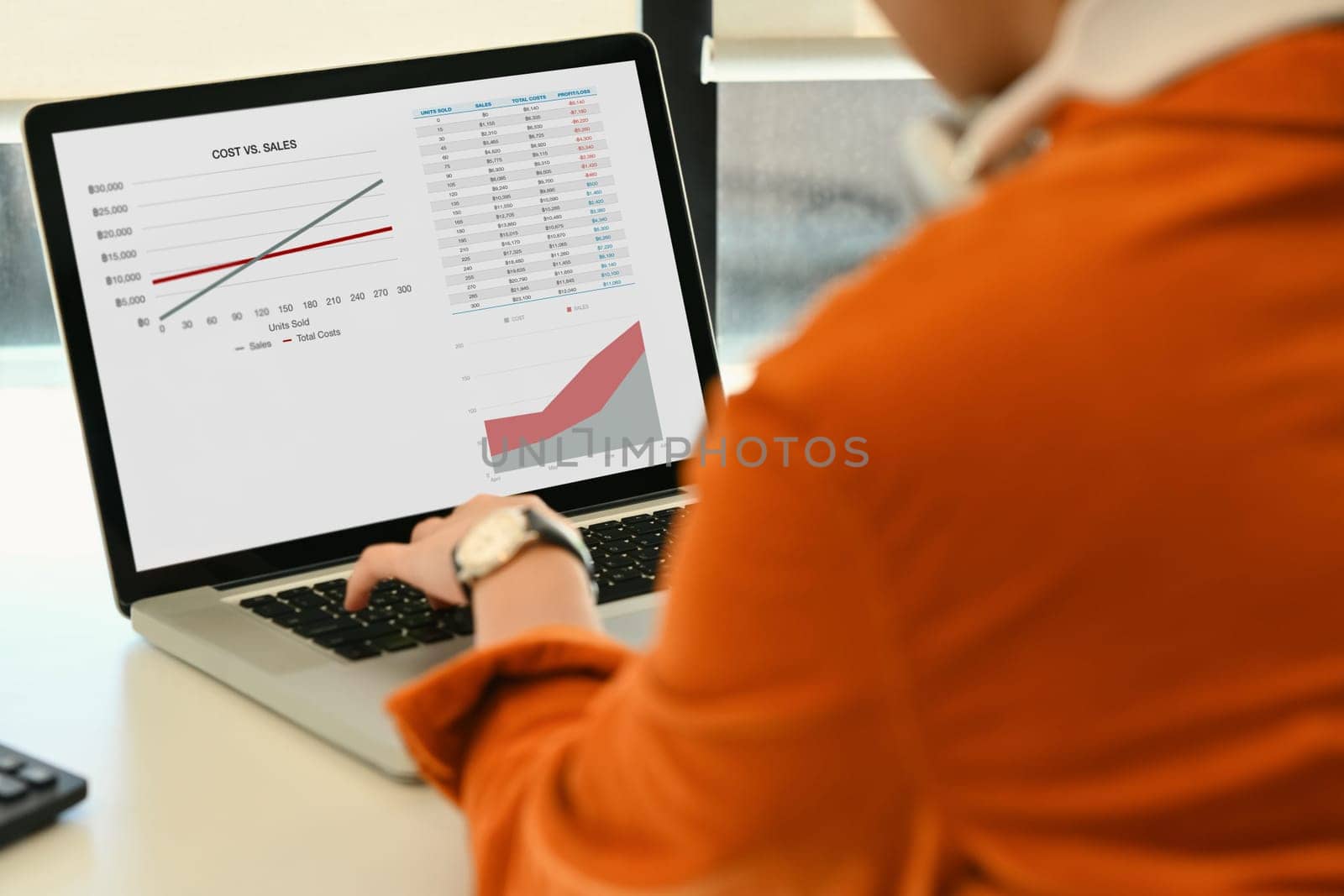 View over shoulder of female economist analyzing sales statistics on laptop at her office desk by prathanchorruangsak