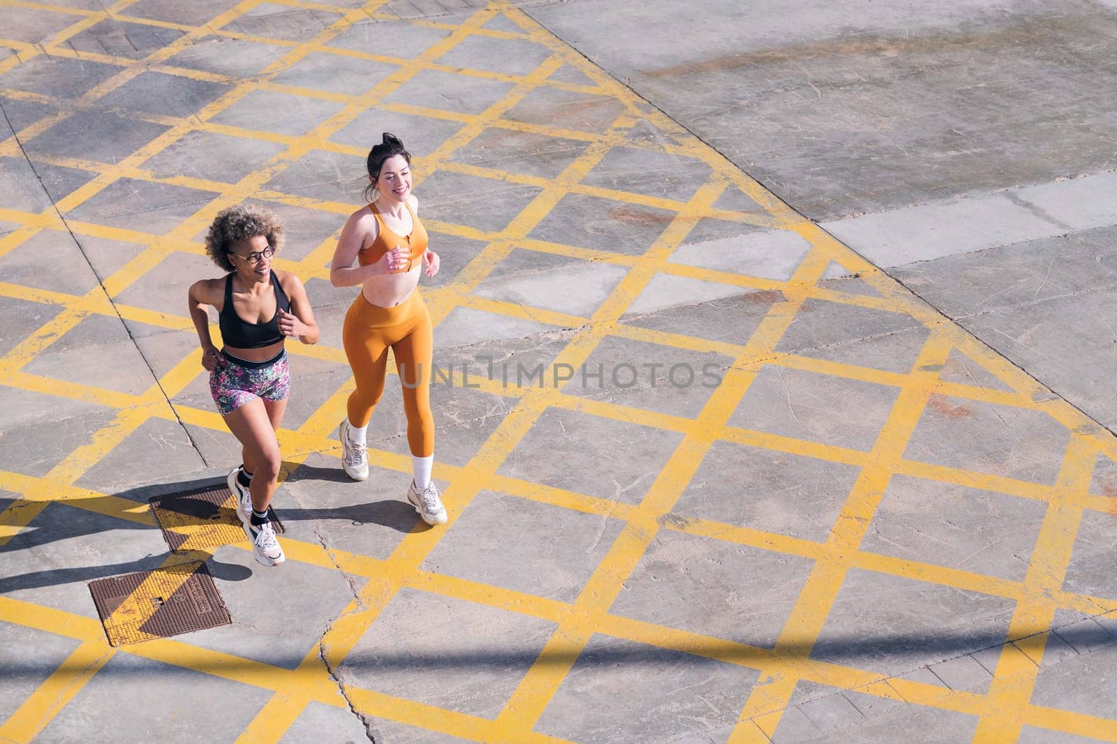 top view of two female friends running happy along city road in a sunny day, concept of friendship and sporty lifestyle, copy space for text