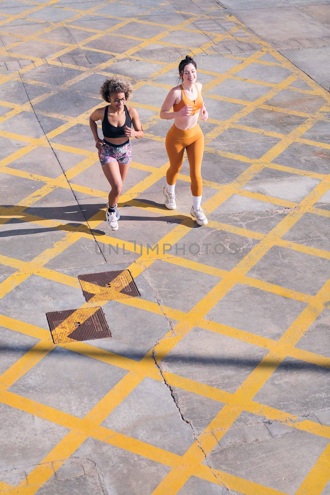 vertical photo of two female friends running happy along city road in a sunny day, concept of friendship and sporty lifestyle, copy space for text