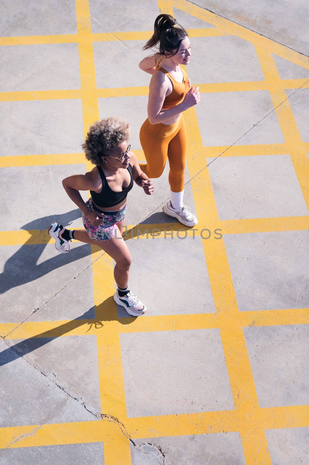 vertical photo of two female friends running happy along city road in a sunny day, concept of friendship and sporty lifestyle, copy space for text