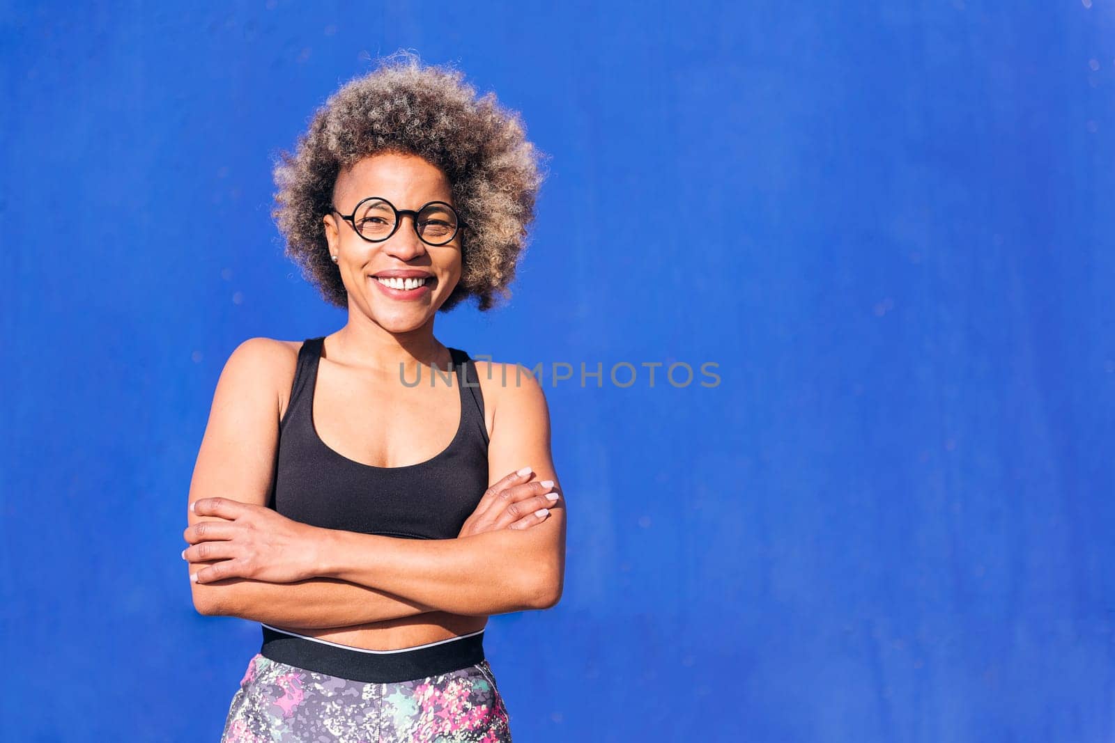 portrait of a smiling african american sportswoman in a blue background outdoors in a sunny day, concept of real people and sporty lifestyle, copy space for text