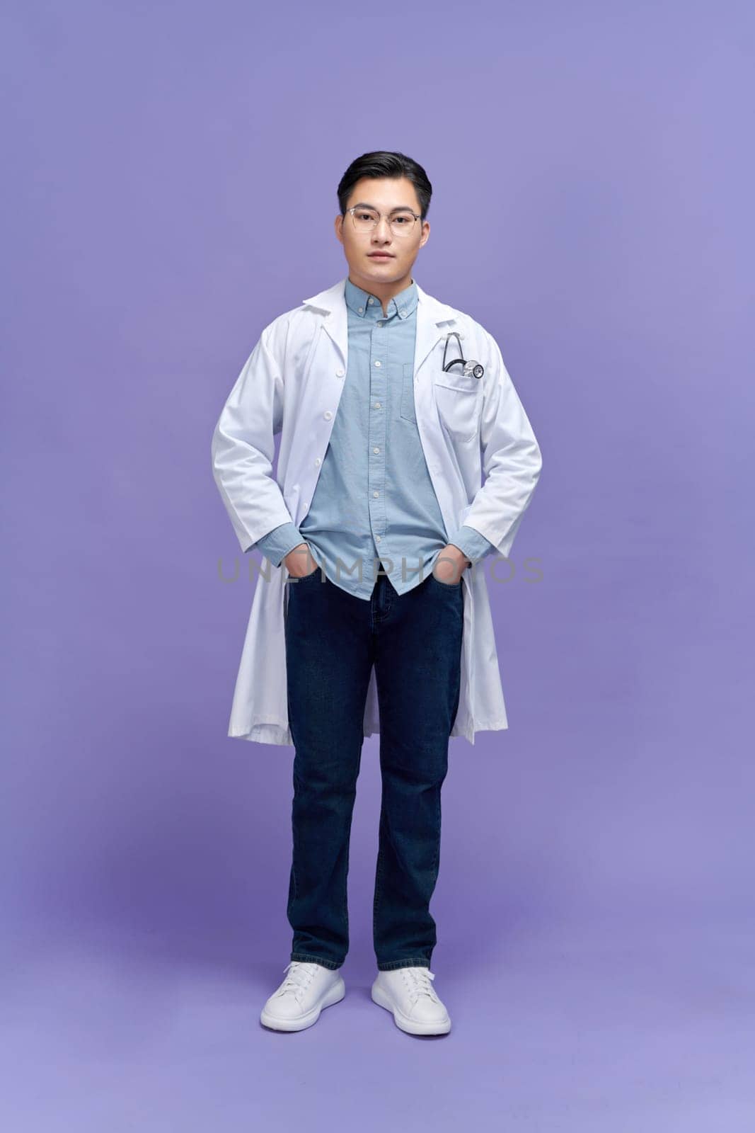 Handsome young doctor in a dressing gown with a stethoscope on a purple background