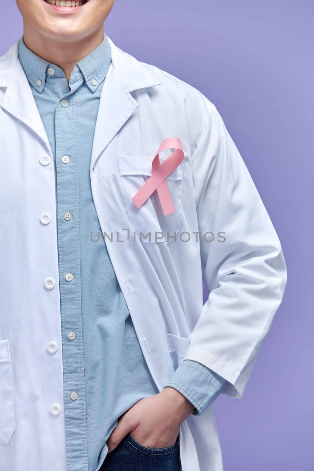 Handsome young doctor with arms crossed against pink