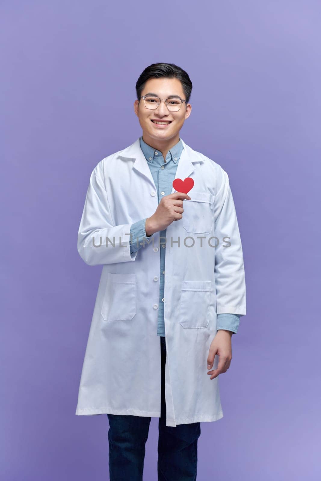Handsome young doctor man holding paper with red heart, very happy pointing with hand and finger