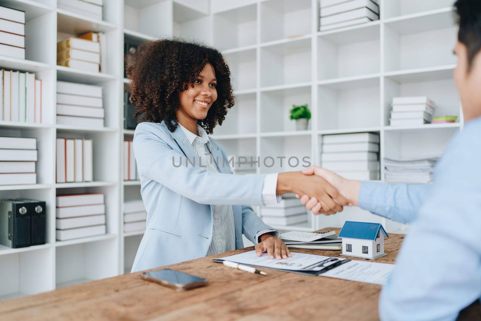 The bank's Female African american Mortgage Officers shake hands with customers to congratulate them after signing a housing investment loan agreement by Manastrong