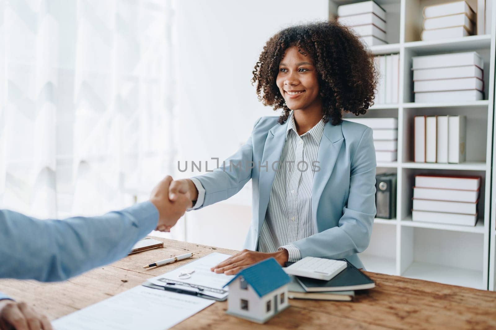 The bank's Female African american Mortgage Officers shake hands with customers to congratulate them after signing a housing investment loan agreement by Manastrong