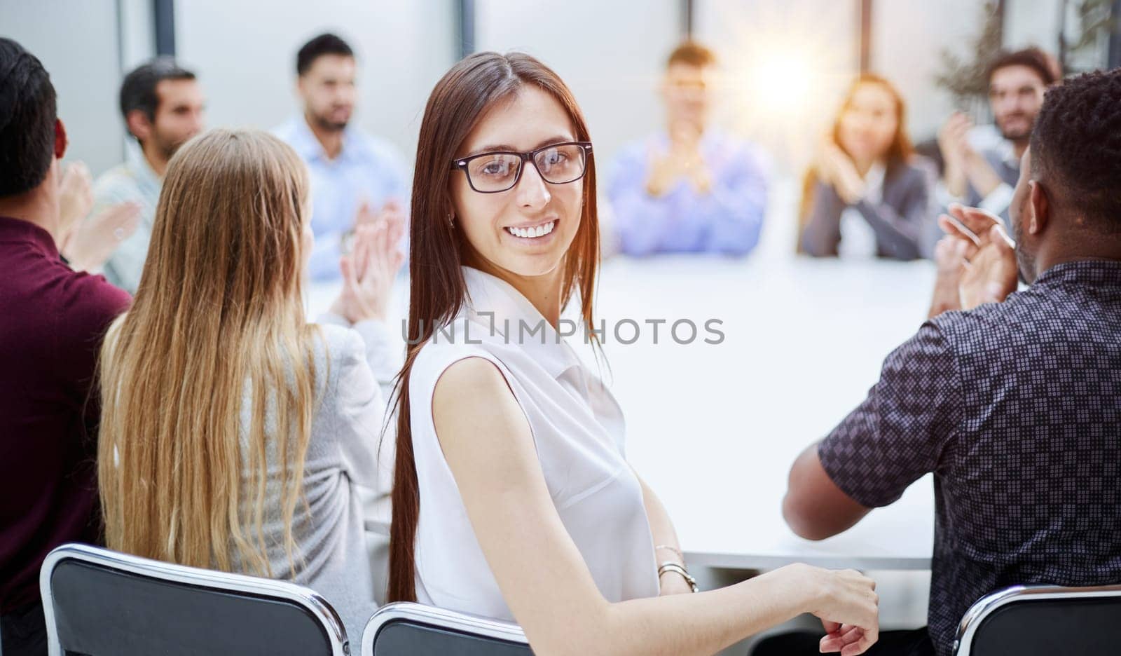 girl posing for the camera sitting at a round table against the background of her colleagues