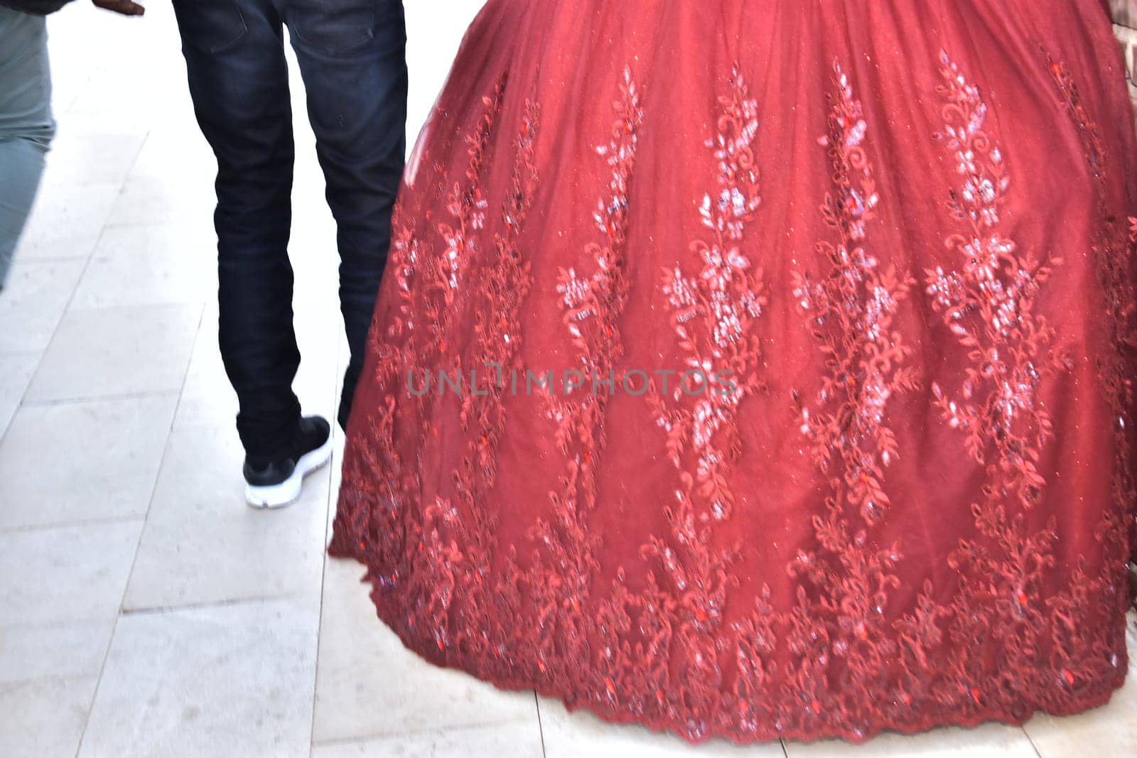 The hem of the lush red wedding dress of the bride and the legs of the boyfriend of the groom in black jeans, newlyweds. High quality photo