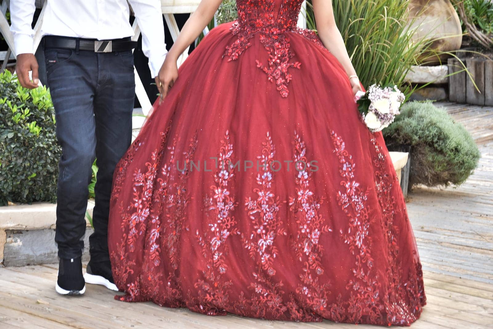 Newlyweds on the street, the bride in a scarlet dress, the groom in a white shirt, no faces. High quality photo