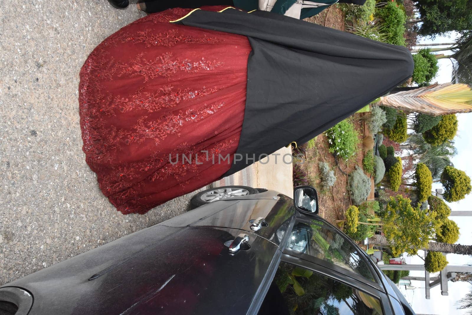 arabic girl bride in a scarlet wedding dress and black cape stands with her back on the street near a black car. High quality photo