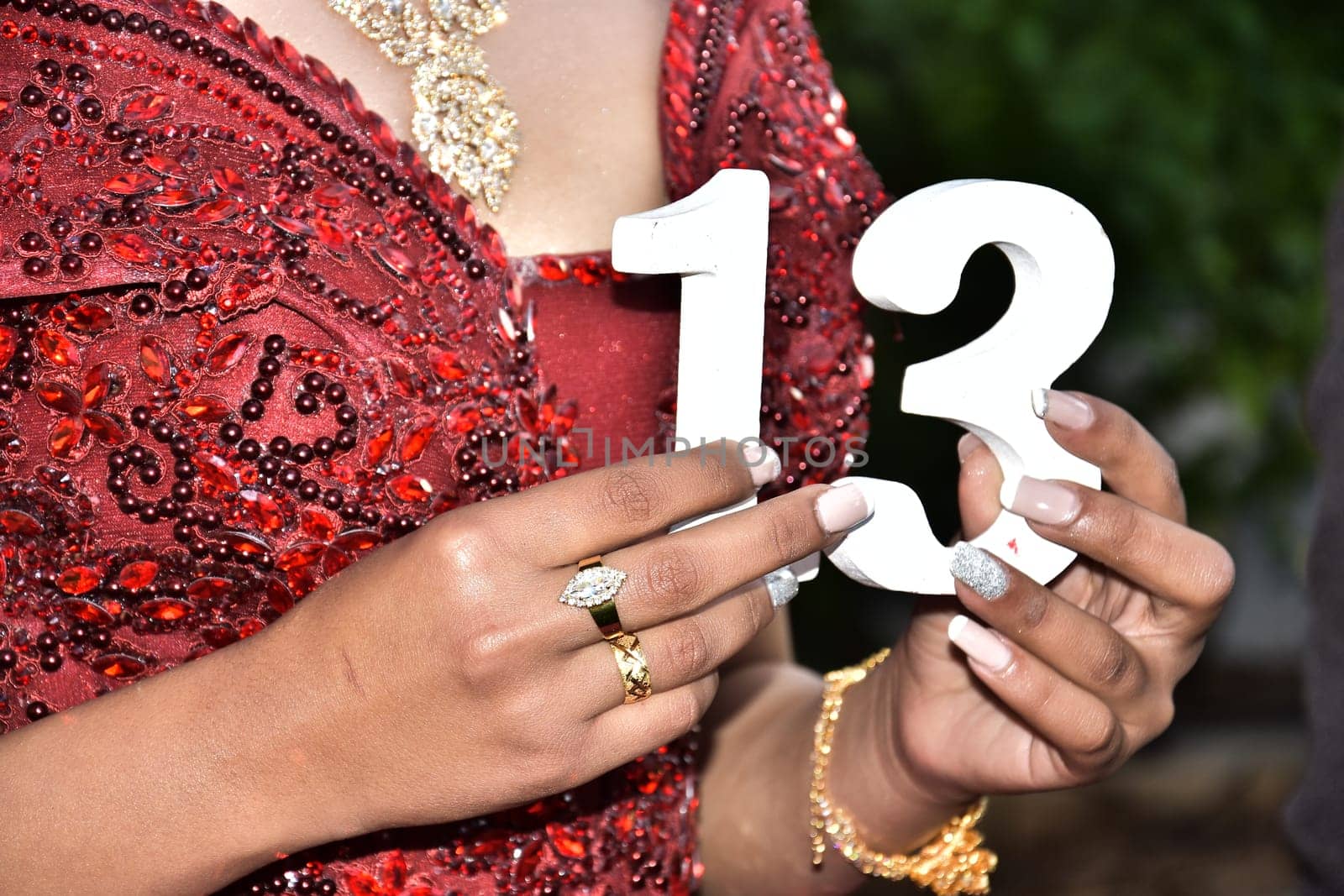 Hands of a girl in a red wedding dress with a white number 13. High quality photo