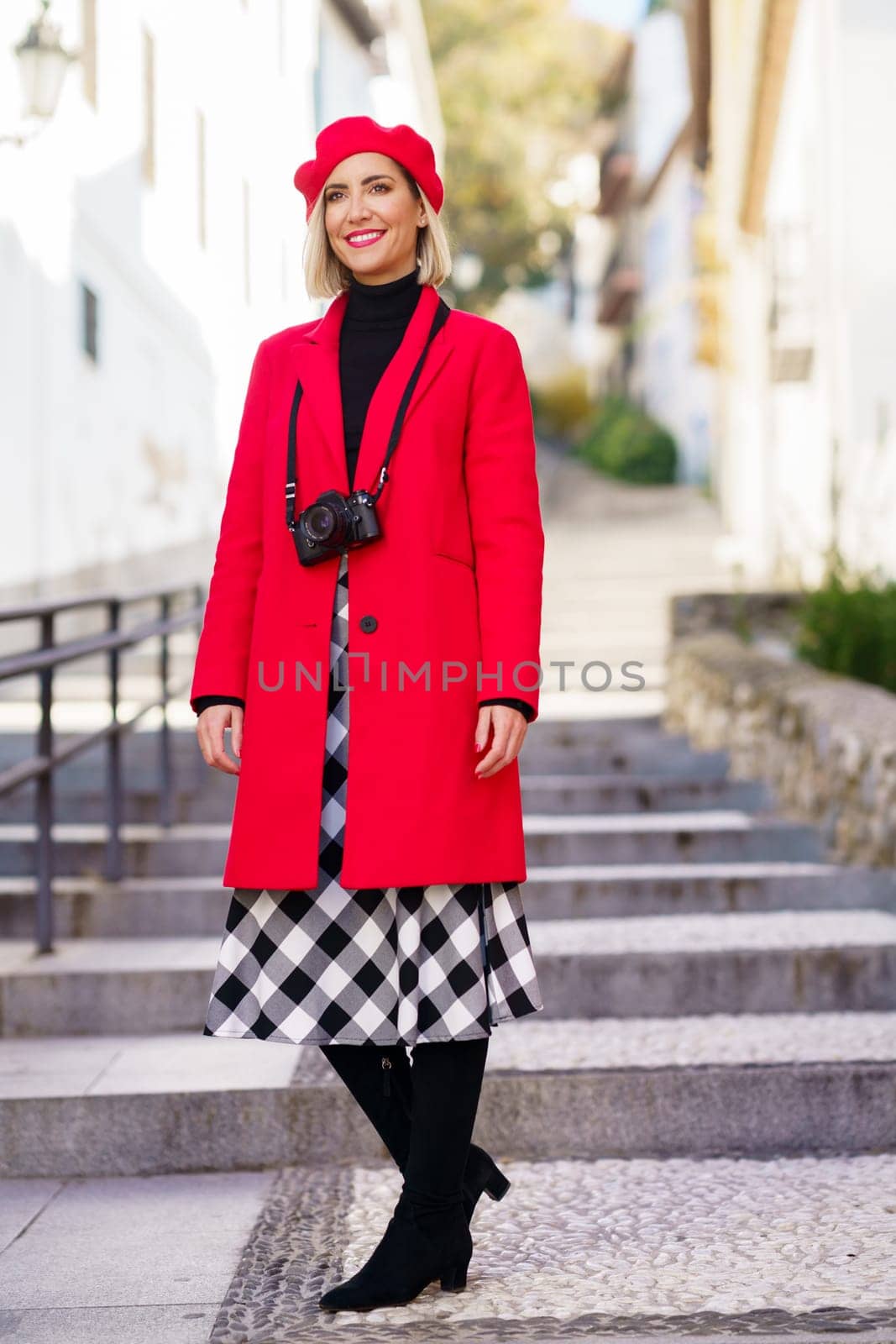 Stylish woman in red coat standing on city street in sunlight by javiindy
