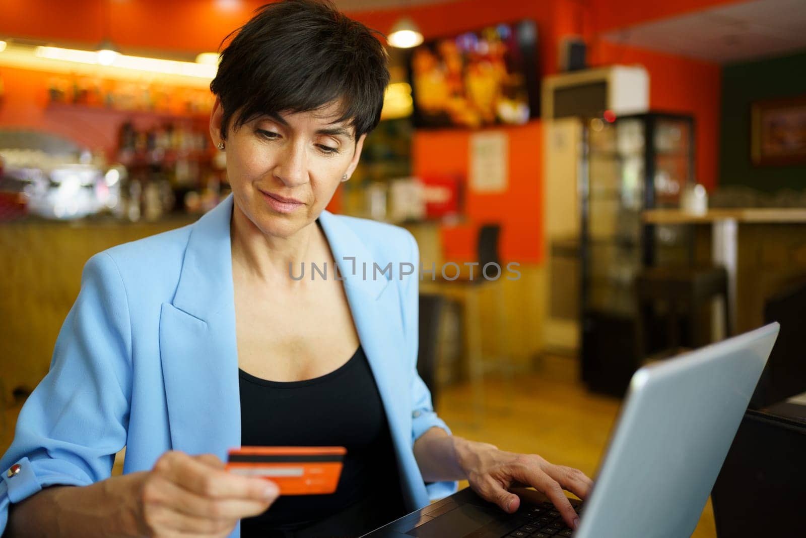Middle age woman using laptop and debit card in cafe by javiindy