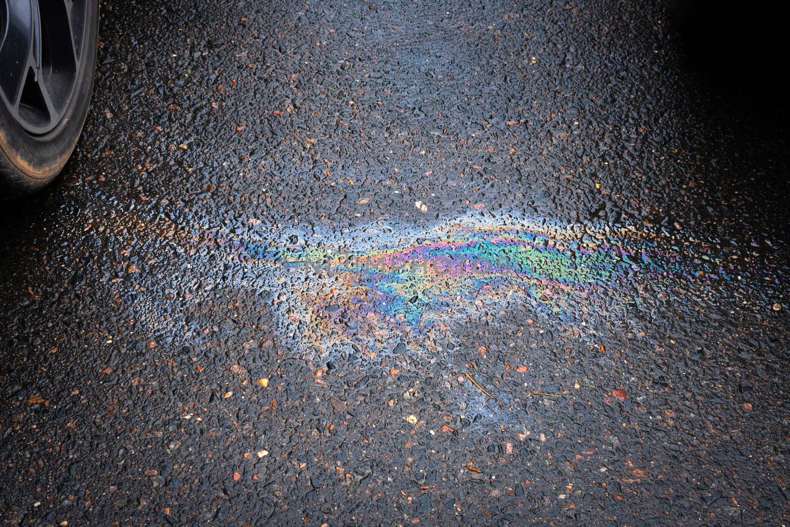 Leakage of oil or gasoline from a car onto a wet asphalt road. The concept of environmental pollution. Selective focus.