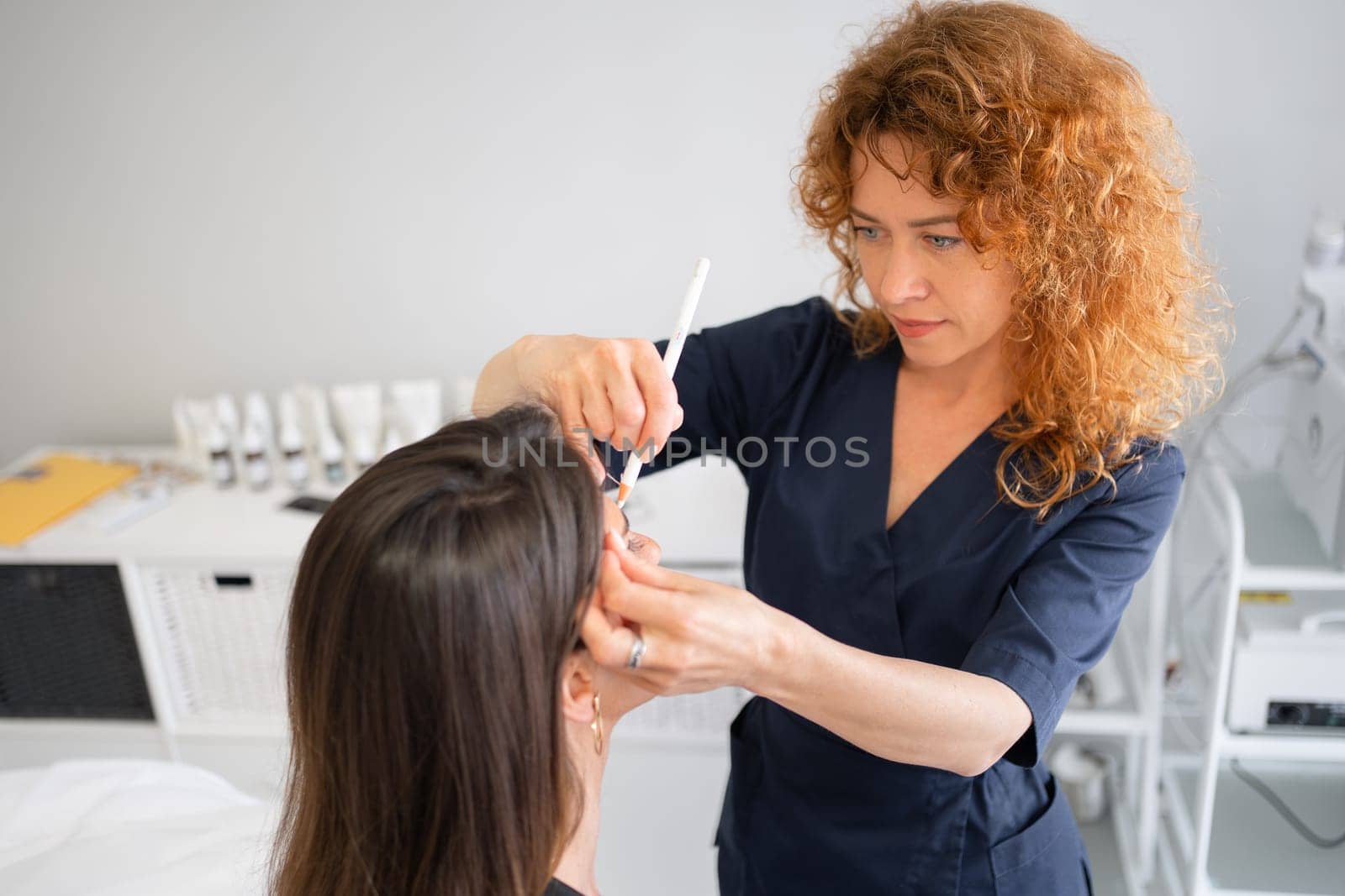 Master applies white markings to correct shape of eyebrow with a special brush. Beautician makes markings with pencil for permanent tattooing. Professional makeup and skin care cosmetology