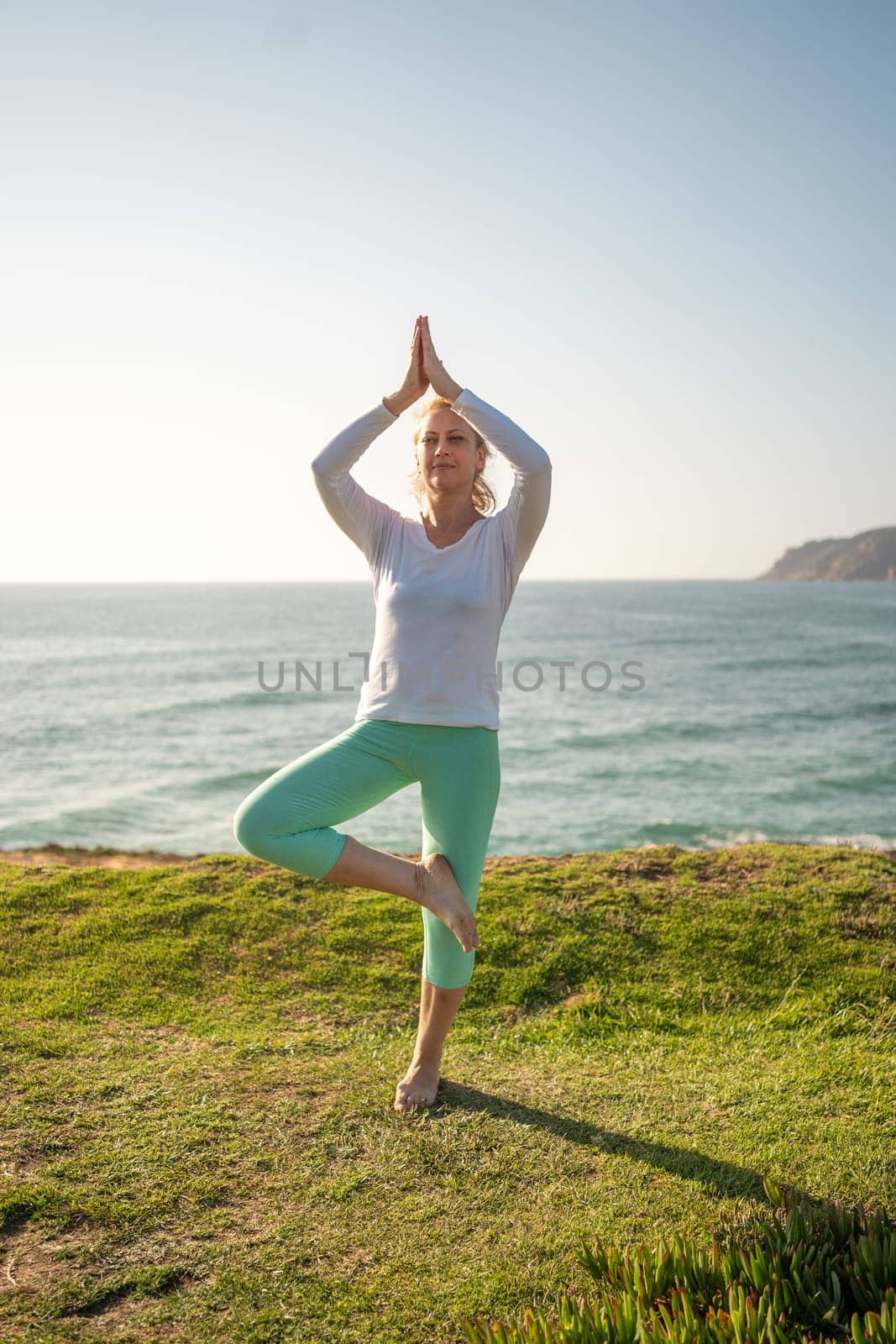 Pensioner woman doing yoga tree pose ocean background by andreonegin