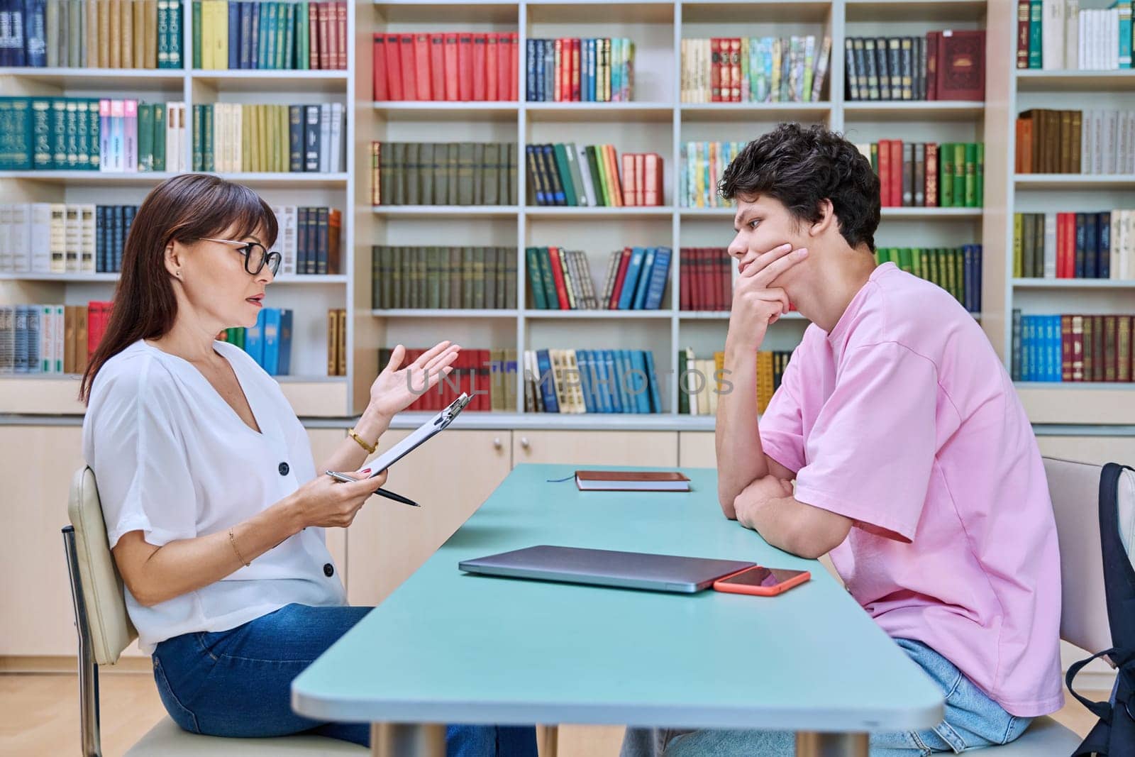 Mature female college counselor, social worker talking with student young male, meeting in library office. Youth mental health, psychology, psychotherapy, help, consultation, mentorship concept