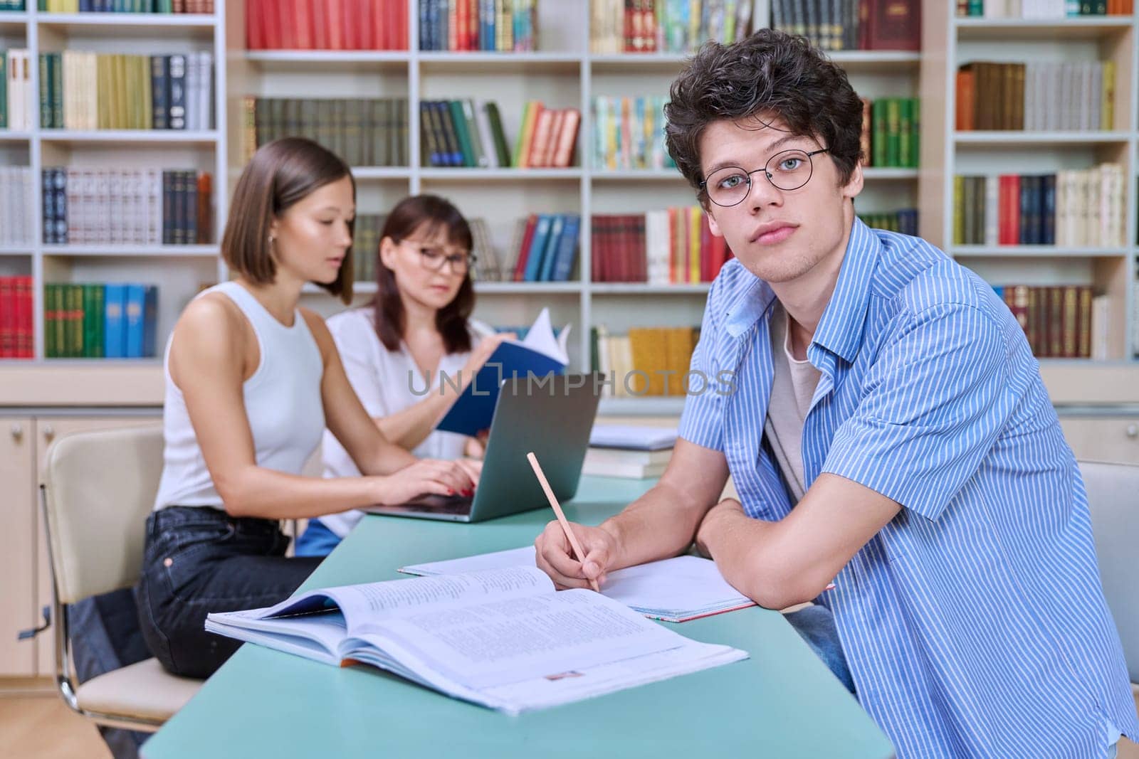 Portrait of student guy at desk inside college library, female student together with teacher preparing for exam. Knowledge, education, youth, college university concept