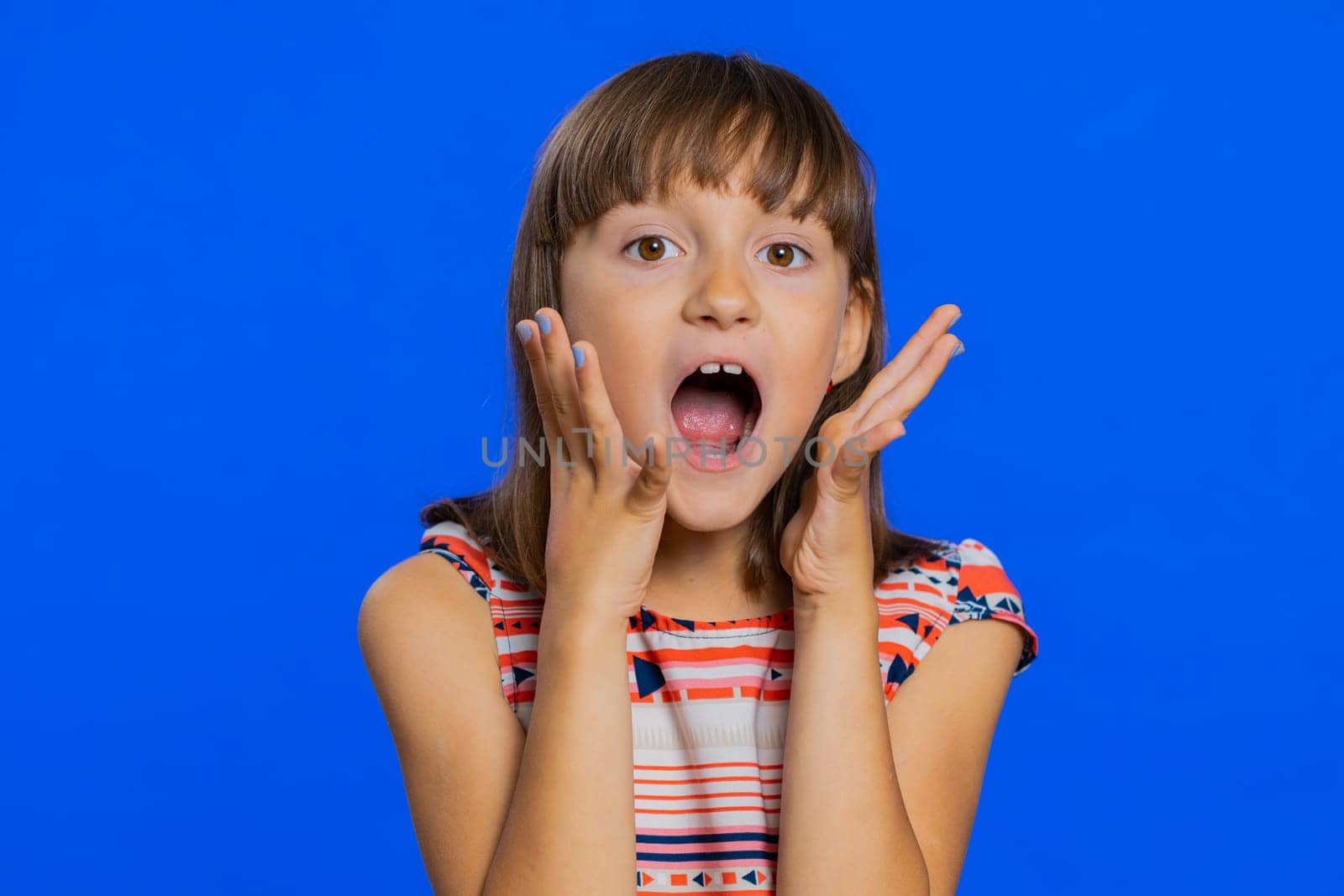 Oh my God, Wow. Young preteen child girl kid looking surprised at camera with big eyes, shocked by sudden victory game winning lottery goal achievemen good news. Children isolated on blue background
