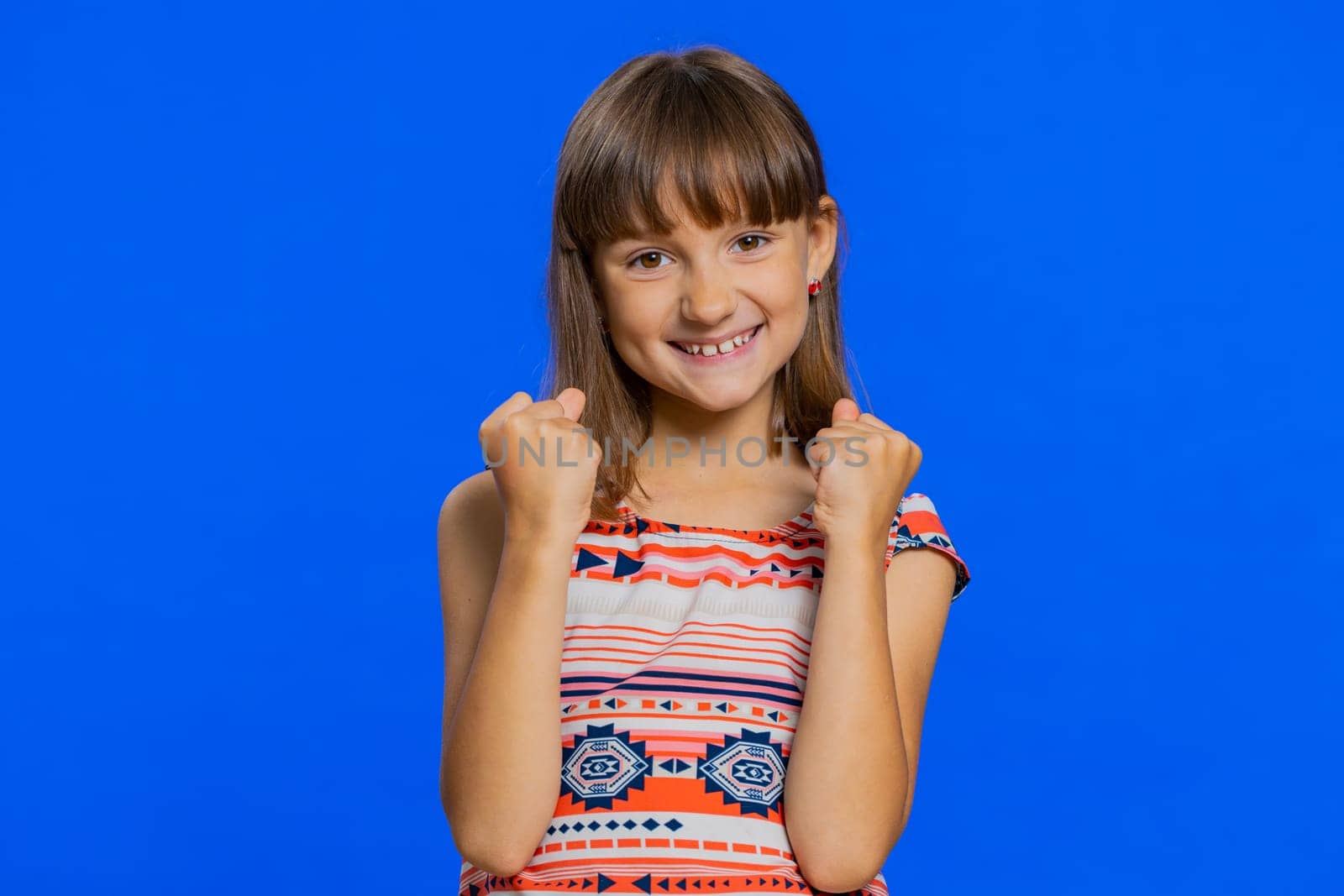 Young preteen child girl kid shouting, raising fists in gesture I did it, celebrating success, winning, birthday, lottery jackpot goal achievemen. Little cute children isolated on blue background