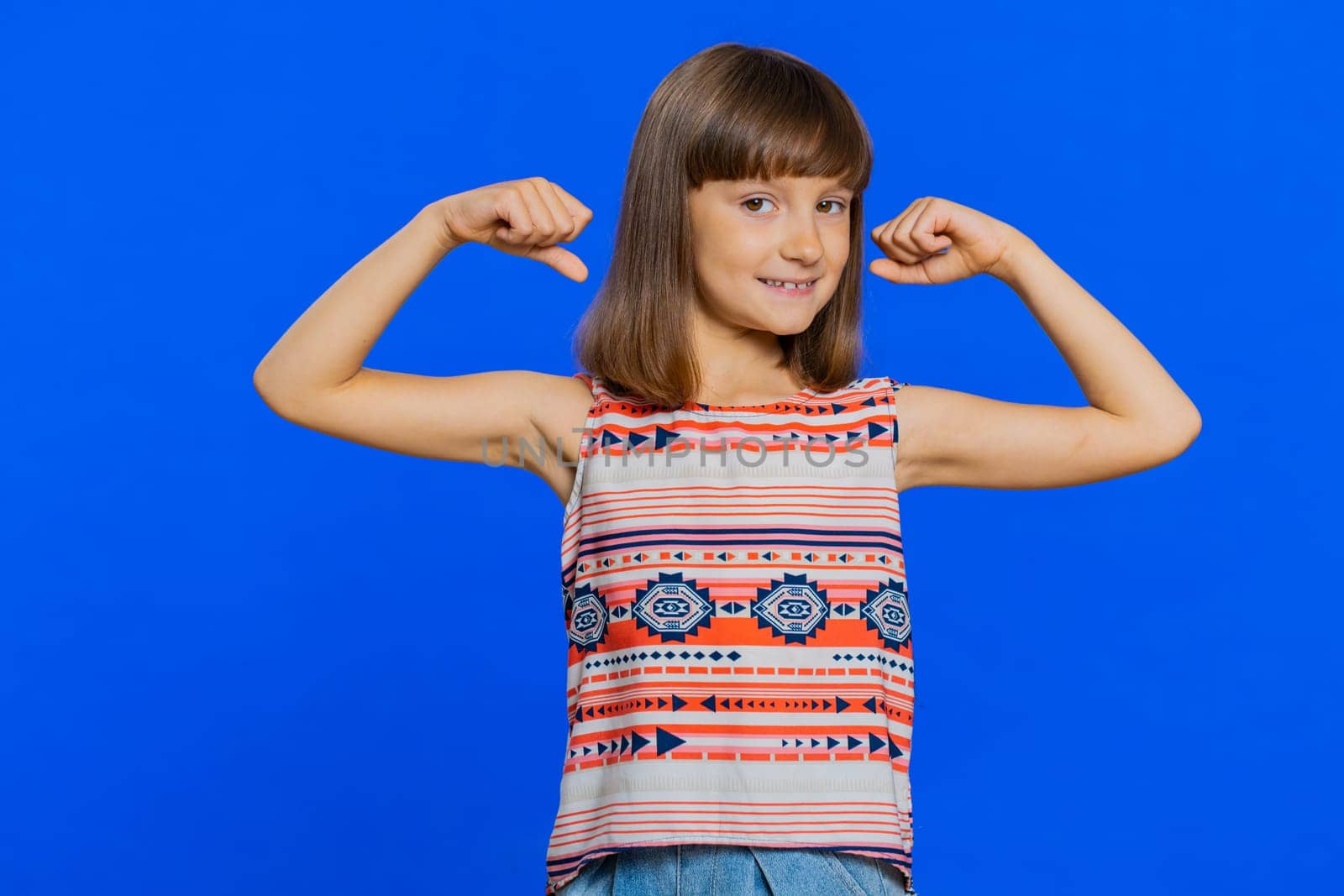I am strong and healthy. Young cute girl showing biceps and looking confident feeling power strength to fight for rights, energy to gain success win. Preteen brunette child kid on blue background