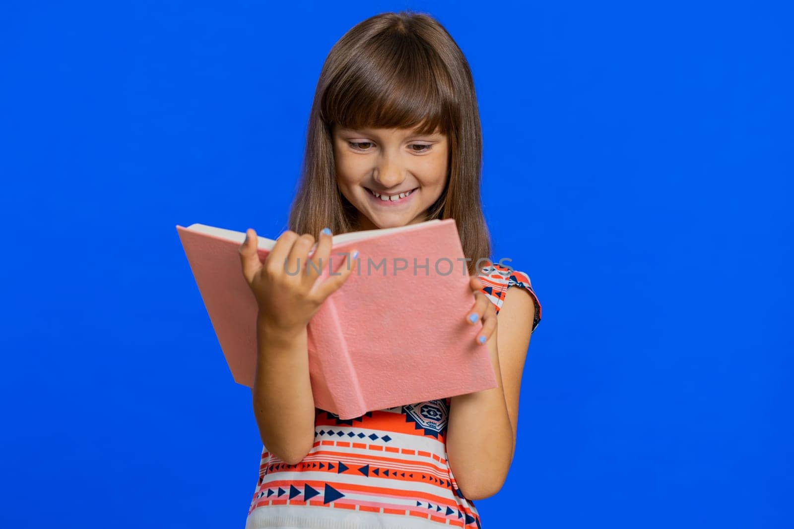 Young school girl reading funny interesting fairytale story book, leisure hobby, knowledge wisdom, education, learning, study, wow. Preteen Caucasian child kid isolated on studio blue background