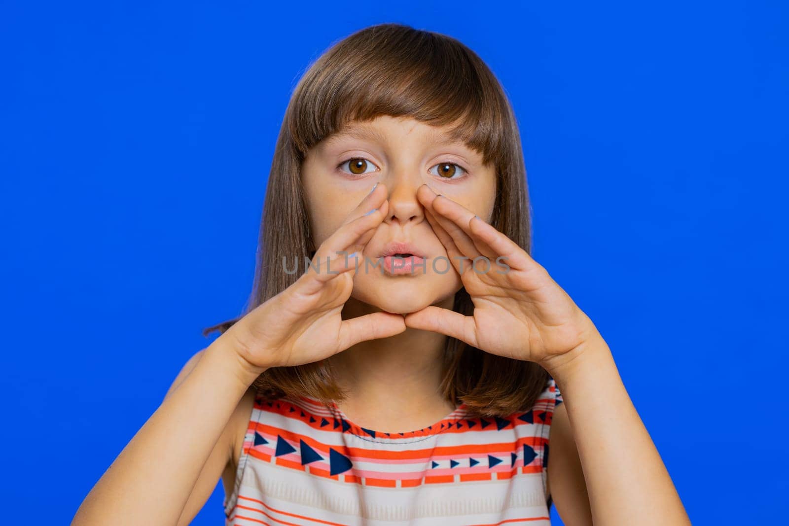 Keep my secrets, silence. Young school girl whisper news rumors holding hands near mouth share gossip quiet. Preteen child kid telling interesting confidential story isolated on studio blue background