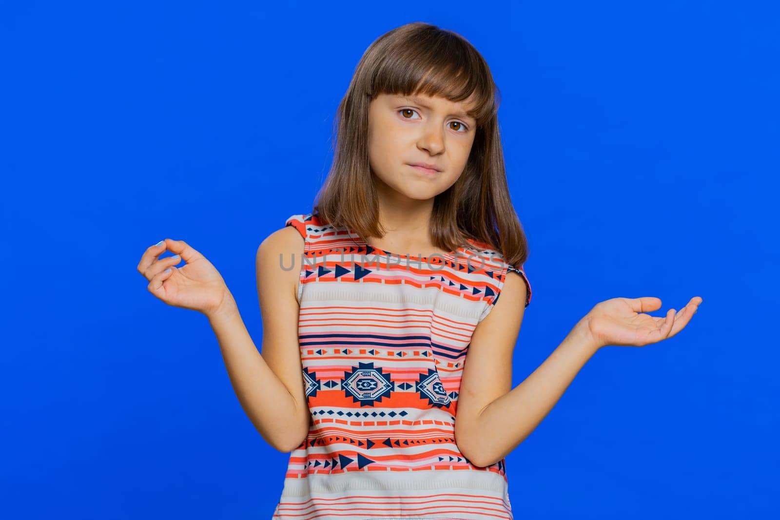 What. Why. Young brunette school girl raising hands in indignant expression, asking why, what reason of failure, demonstrating disbelief irritation by troubles. Preteen child kid on blue background